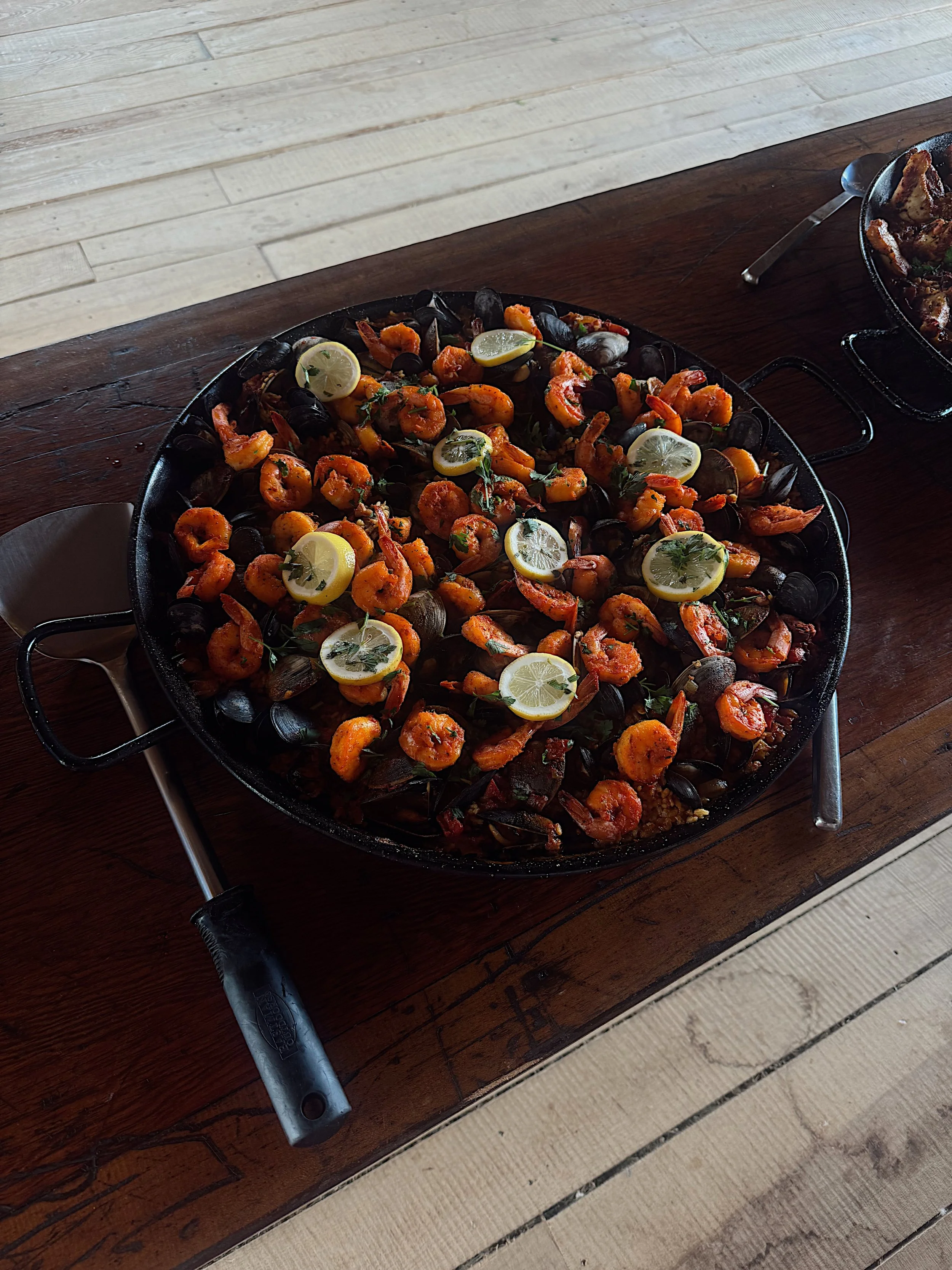 A large cast iron skillet filled with cooked shrimp, lemon slices, and herbs set on a wooden table.