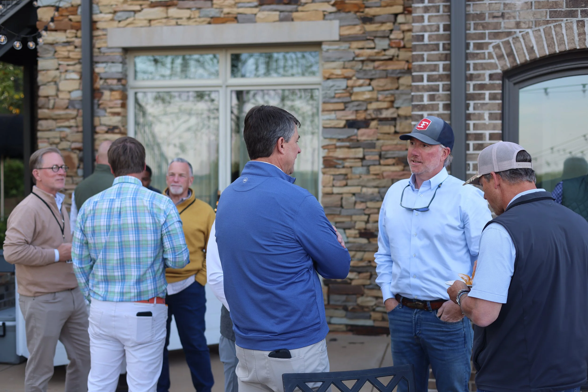 A group of people chatting outside a building with a stone and brick facade.