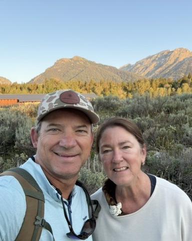 A man and woman taking a selfie outdoors with mountains in the background.
