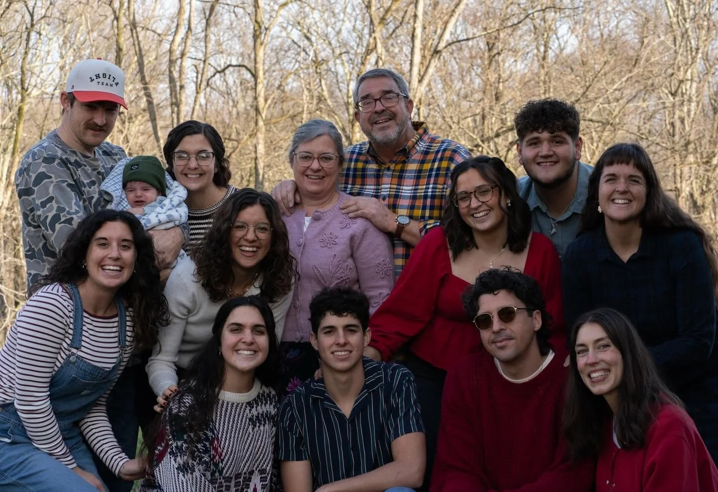 Our Miller family photo outdoors in a wooded area with many smiling members, including a baby, teenagers, and adults, all dressed casually.