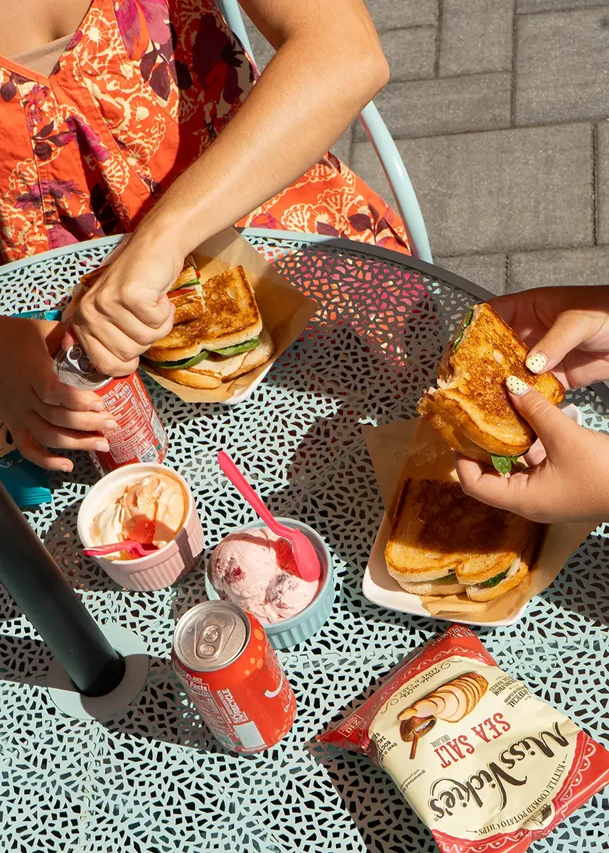 Two people eating grilled cheese sandwiches with potato chips and ice cream on a decorative metal outdoor table.