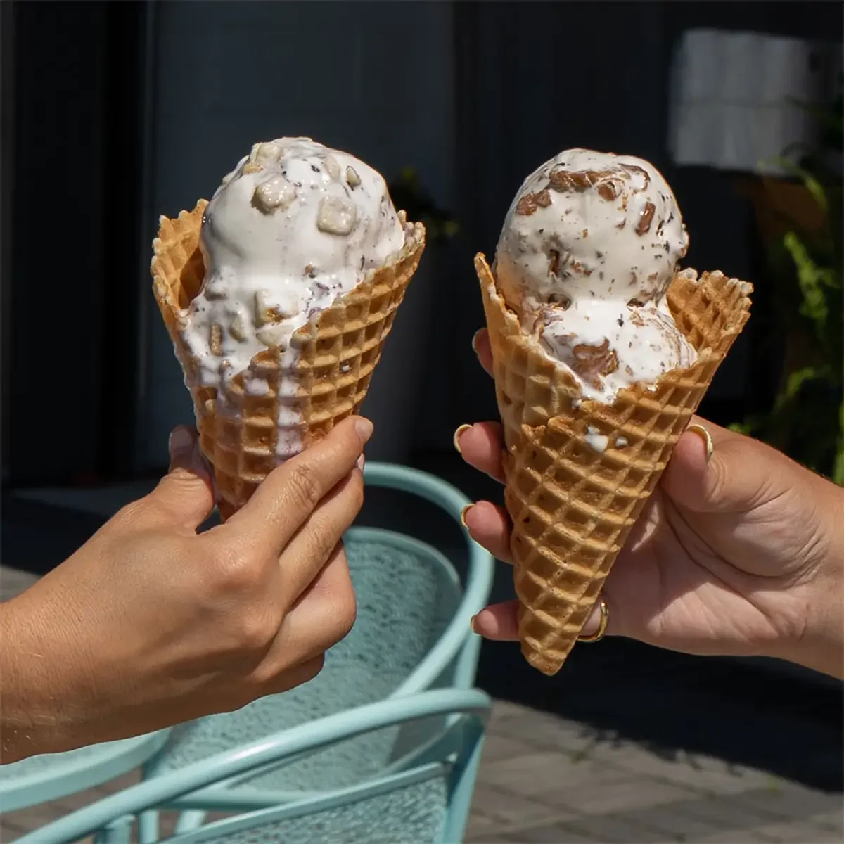 Two people holding waffle cones with scoops of vanilla ice cream sprinkled with chocolate and nuts.