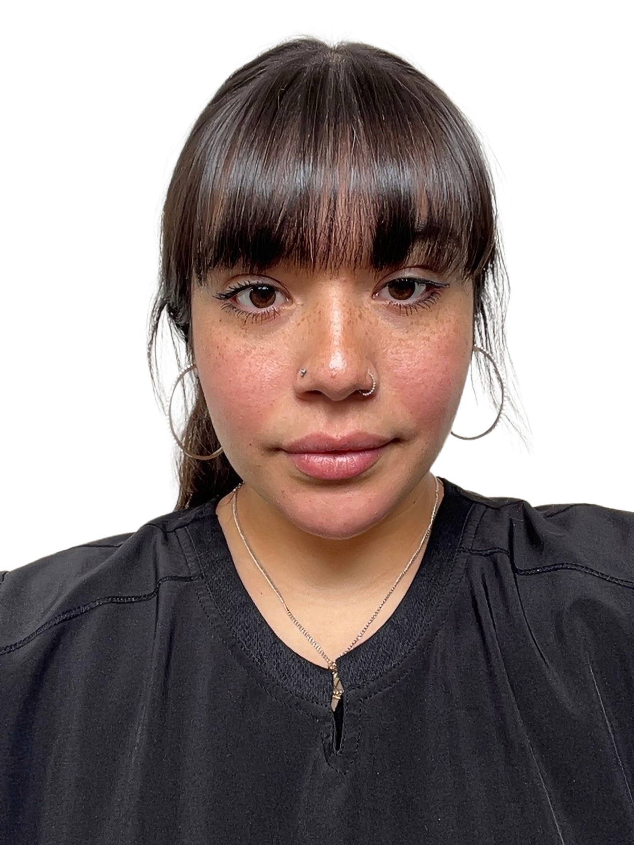 A young woman with brown hair and blunt bangs, wearing silver hoop earrings, a nose ring, a thin necklace, and a black top, smiling softly.