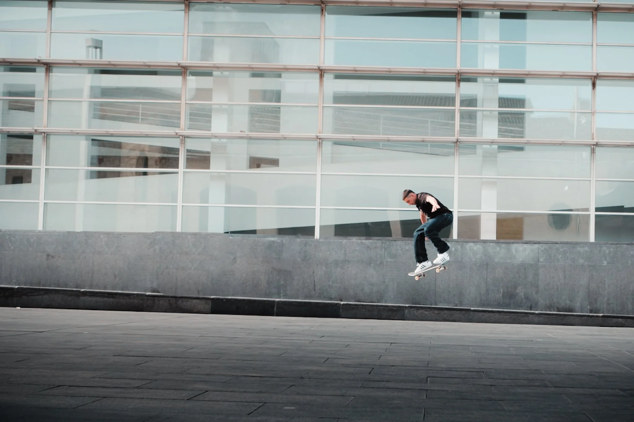 A person skateboarding in front of a modern glass building with reflections of the sky and surroundings.