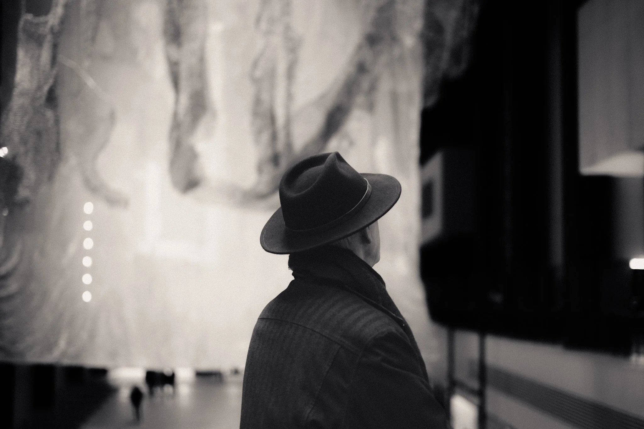 A person is lying on the floor with legs crossed, wearing jeans and a fedora hat, in an indoor setting with a marble floor and indistinct background.