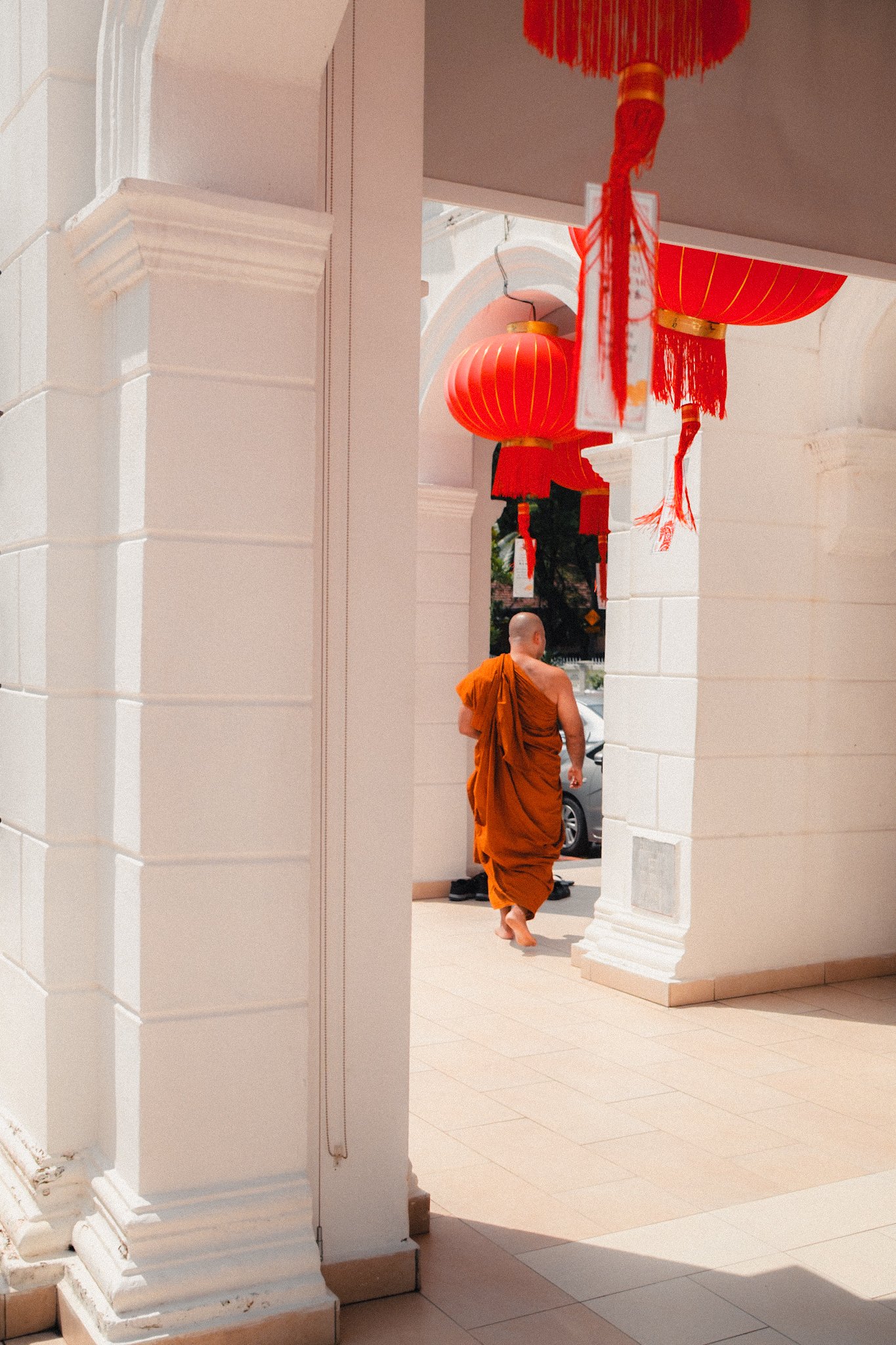 A Buddhist monk in orange robes walking barefoot through an area decorated with red lanterns.