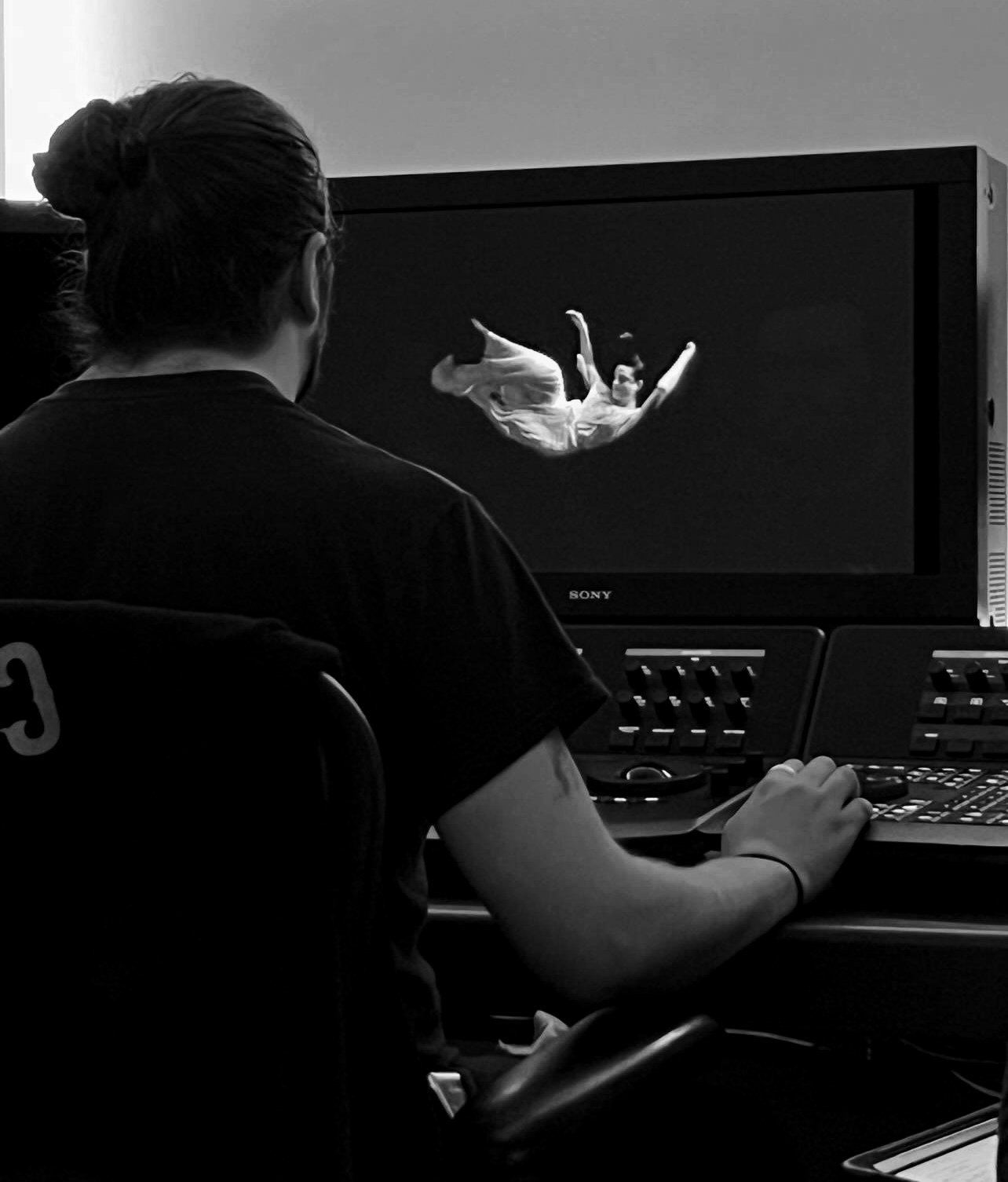 A person working at a computer, colour grading with a monitor displaying an image of a gymnast in mid-air.