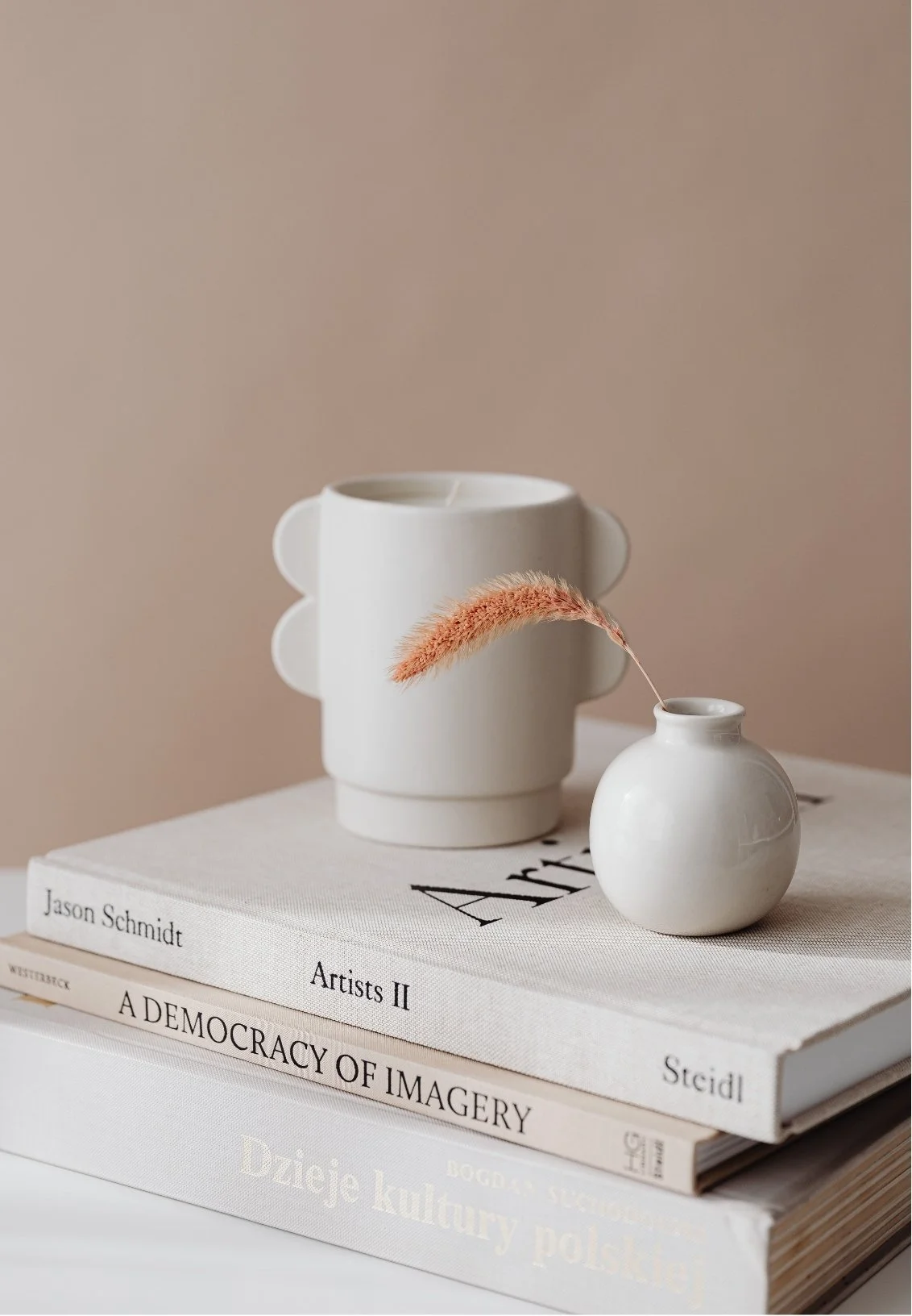 Stack of art books with a white smiling face vase holding a pink dried flower on top