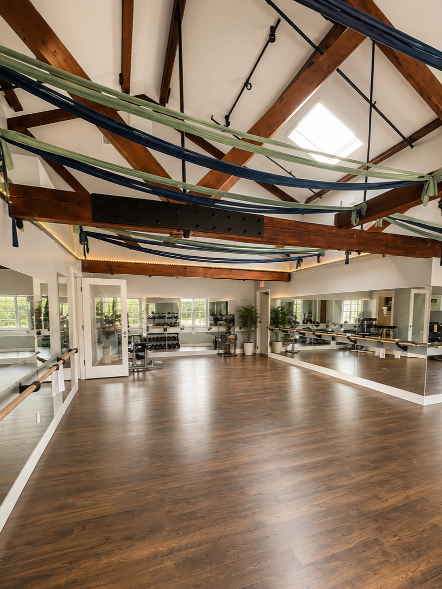 Empty fitness studio with wooden floors, large mirrors, and ballet barres, decorated with green and blue fabric hanging from the ceiling beams.