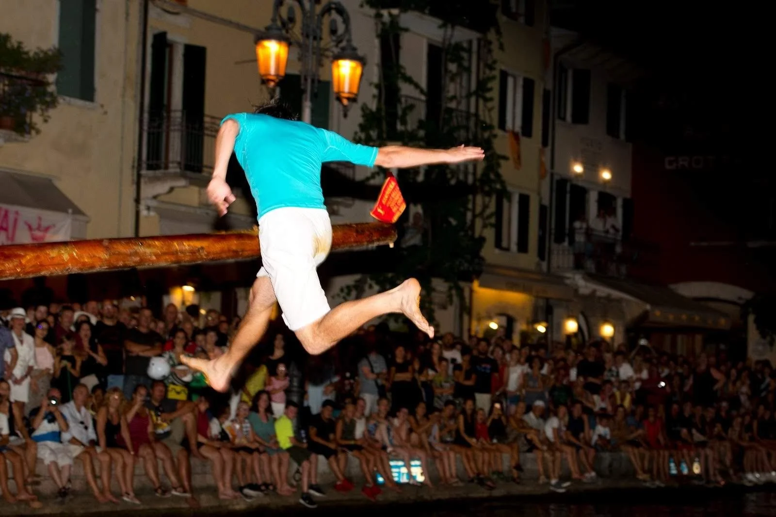 Persona che partecipa a un spettacolo tradizionale, che attraversa un palo durante la notte, con un pubblico numeroso che guarda.