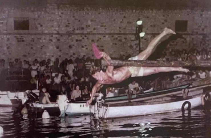 Persone che fanno acrobazie su un motoscafo in acqua di notte con pubblico in tribuna dietro.
