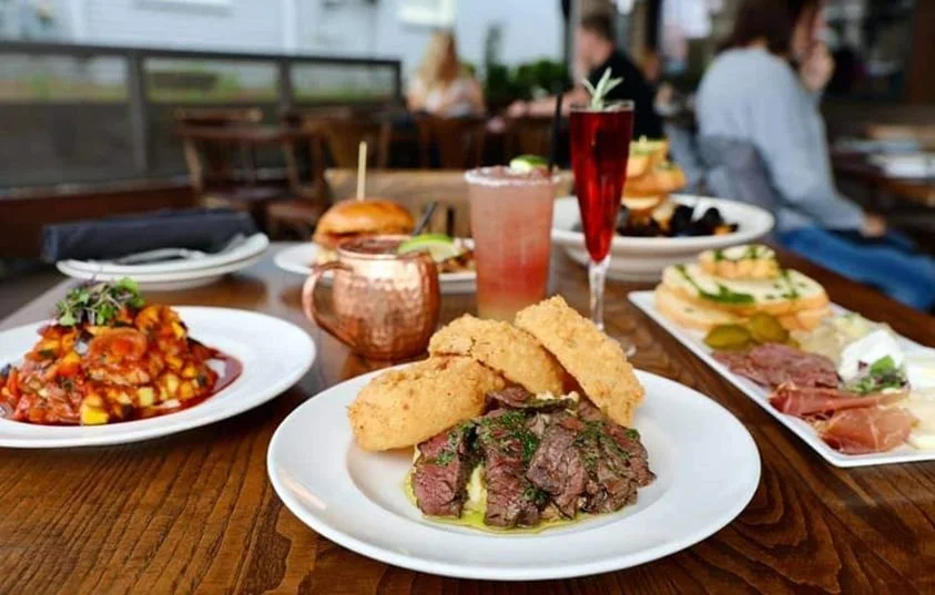 A table with various dishes including fried steak, breaded chicken, pasta with sauce, sandwiches, and drinks at a restaurant