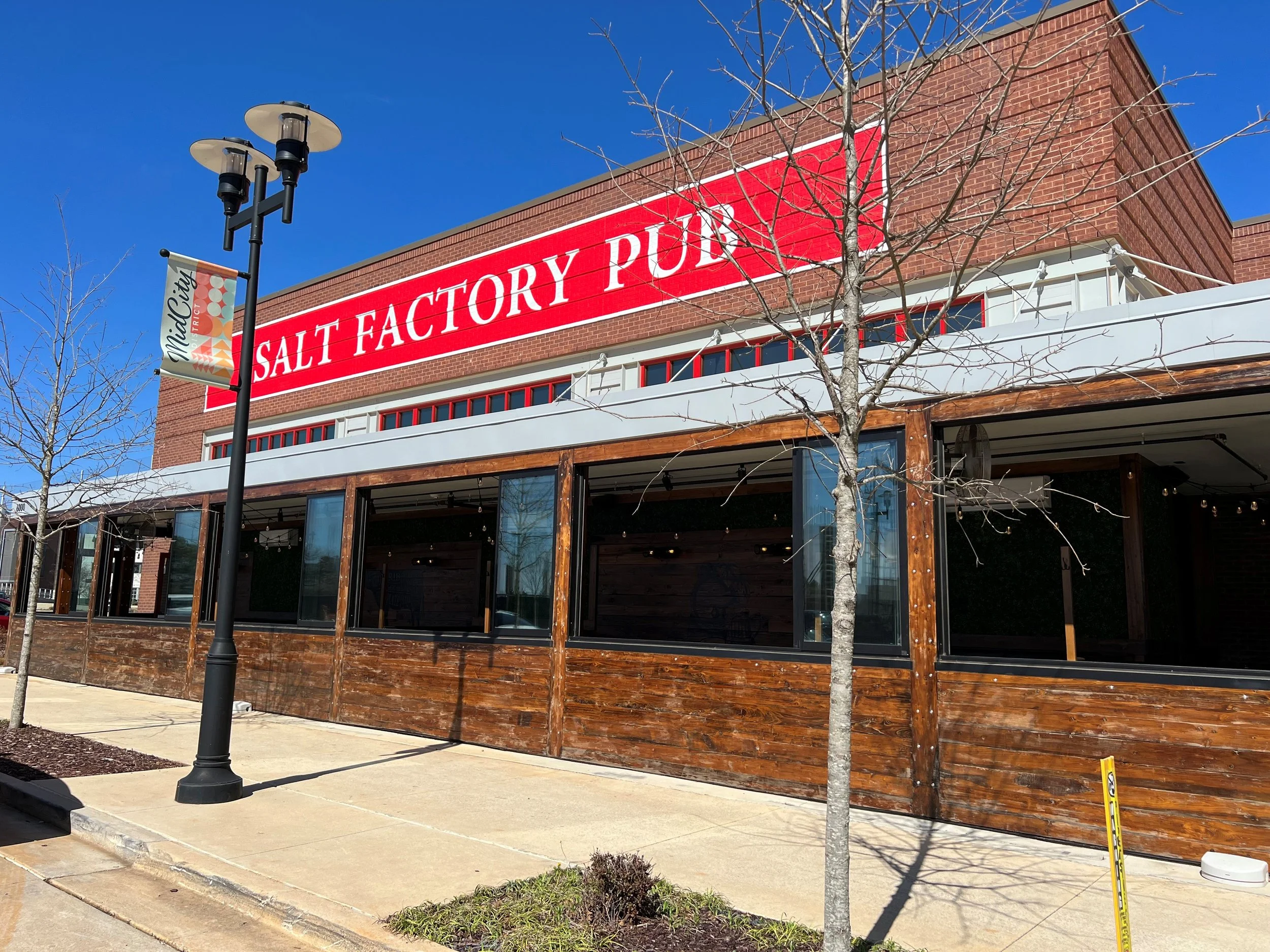 Exterior of a brick building with a sign reading 'Salt Factory Public' and a streetlamp in front, under a clear blue sky.
