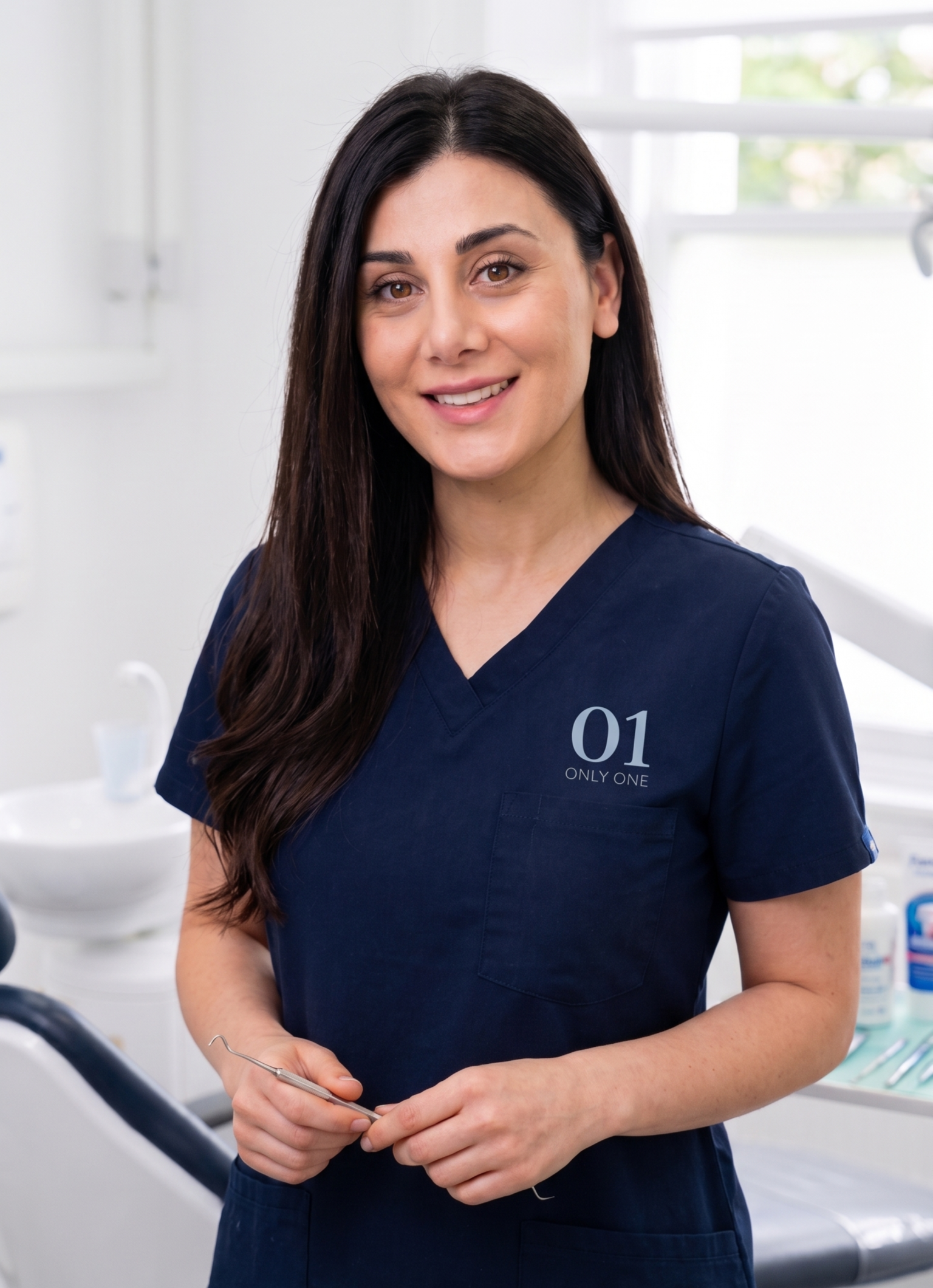 A woman in navy blue scrubs holding dental instruments in a dental office.