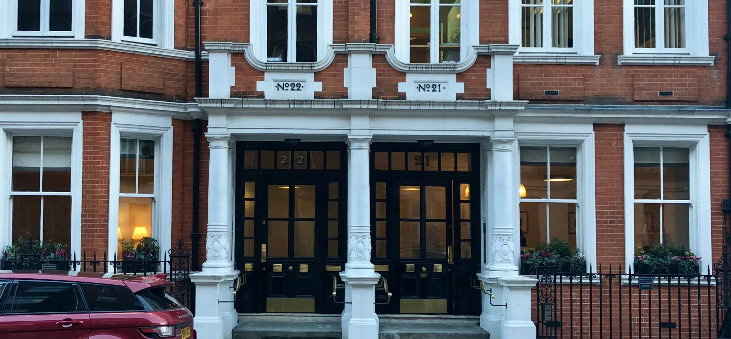 Front view of Only One Clinic at 21 Wimpole Street Marlybone, a red brick building with white architectural details, bay windows, and a gated entrance, with a red car parked in front.