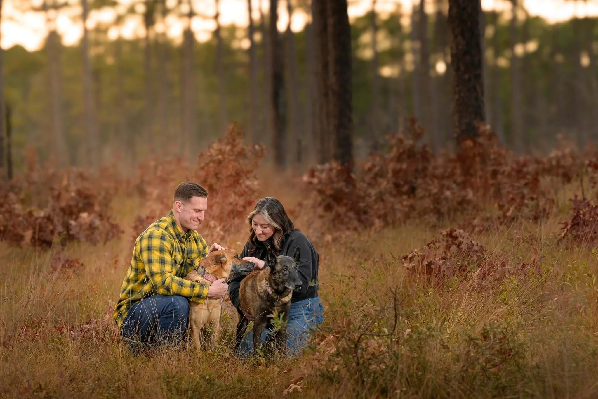 Tom and Carly kneeling in autumn grass among longleaf pines with Cri and Bailey in eastern North Carolina.