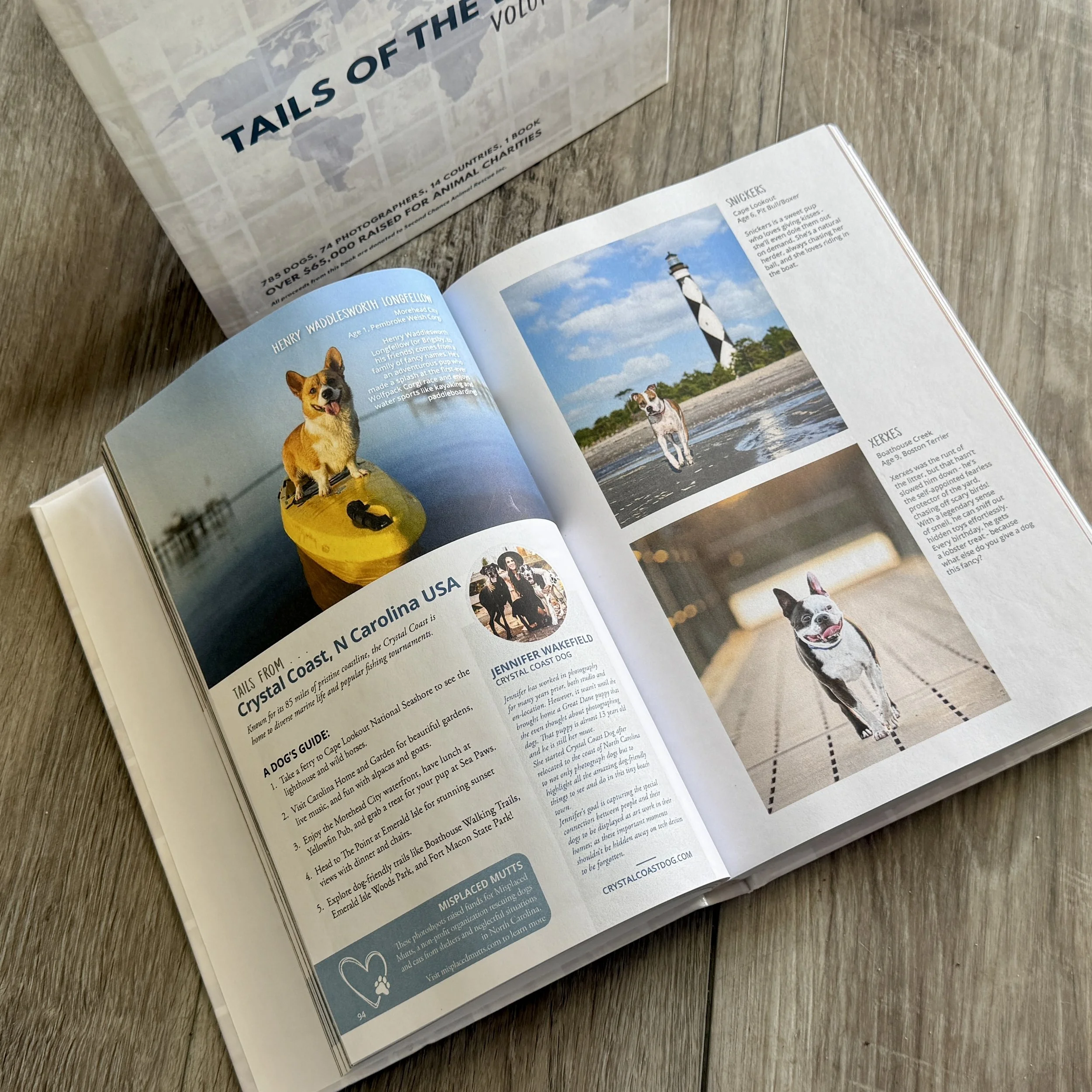 Open magazine featuring dog photography and profiles from Crystal Coast, North Carolina, beside a cover reading “Tails of the World” on a wood table.