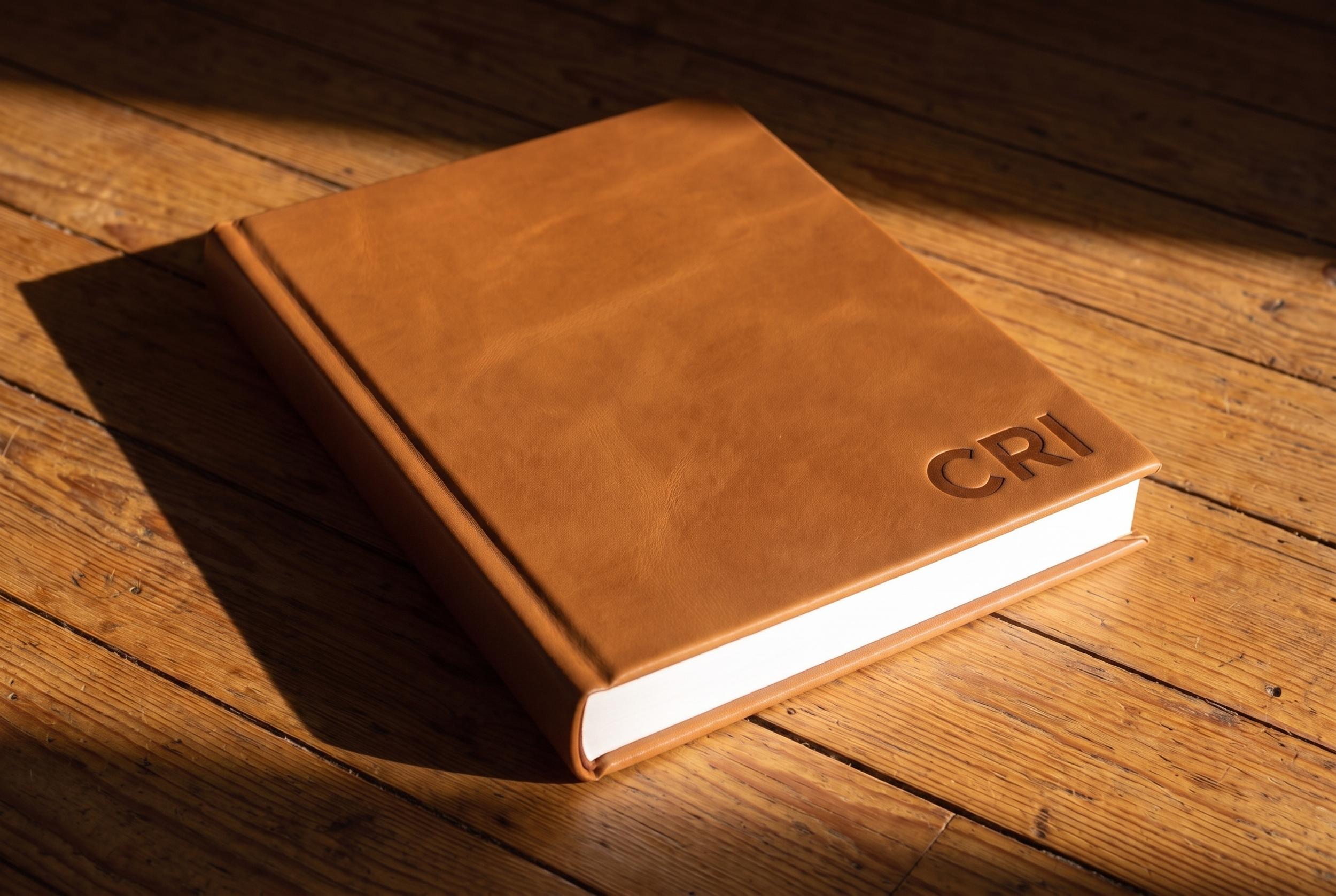 Tan leather heirloom album with Cri's name pressed into the cover, resting on a wood floor in window light.