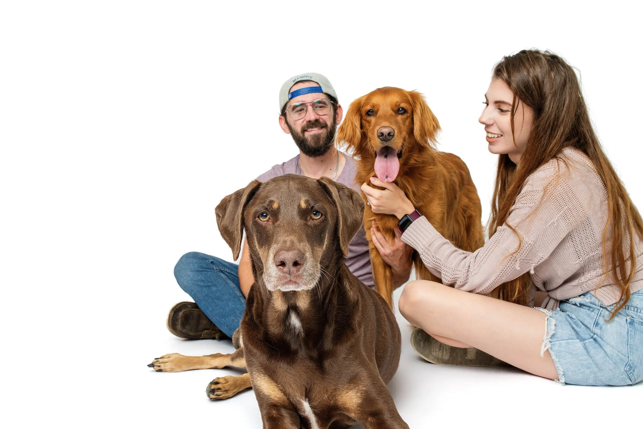 Hank, a chocolate German Shorthaired Pointer and Labrador mix, lies in the foreground staring straight at the camera while his family sits behind him holding Lilah.