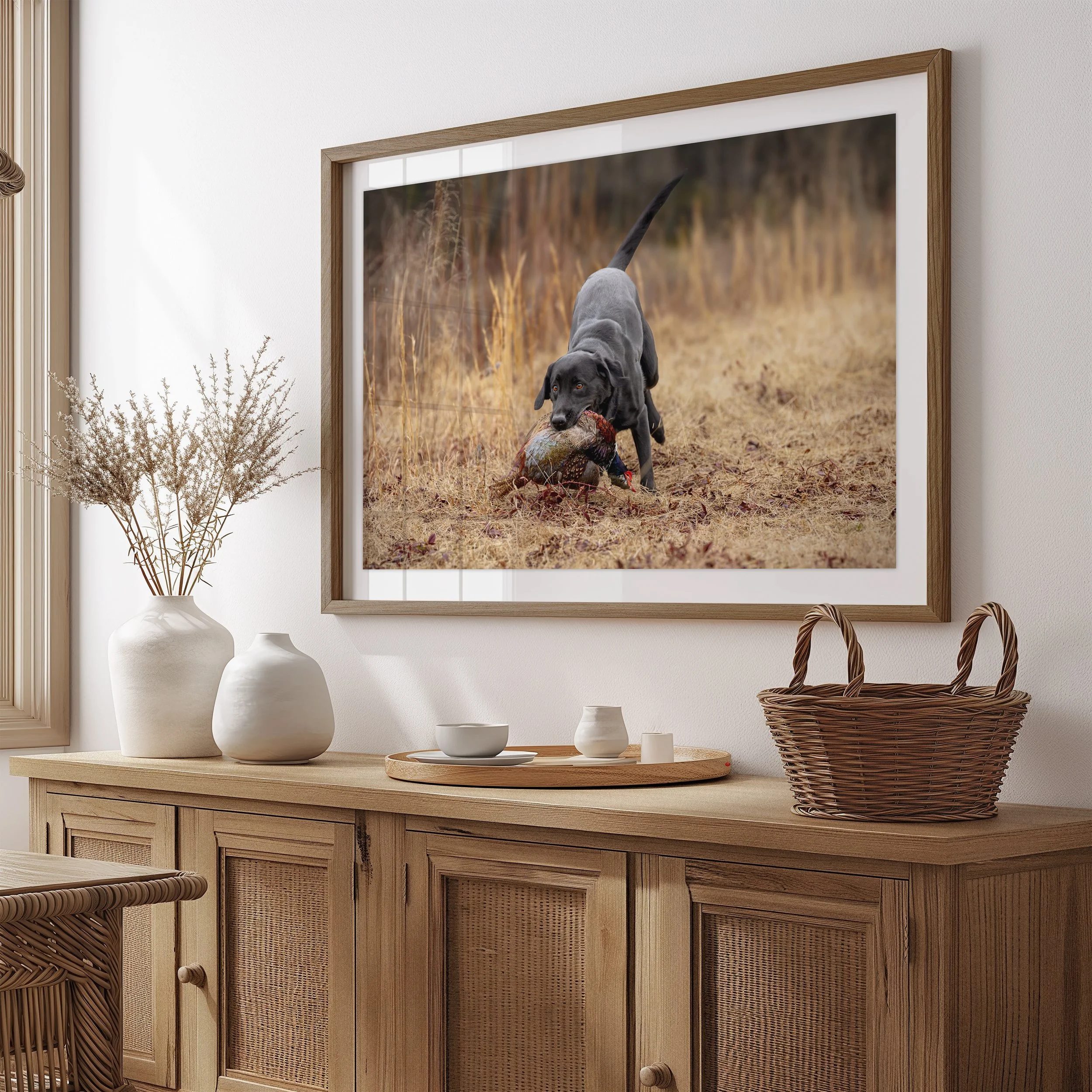 Framed photograph of a black hunting dog retrieving a pheasant above a rustic wooden sideboard