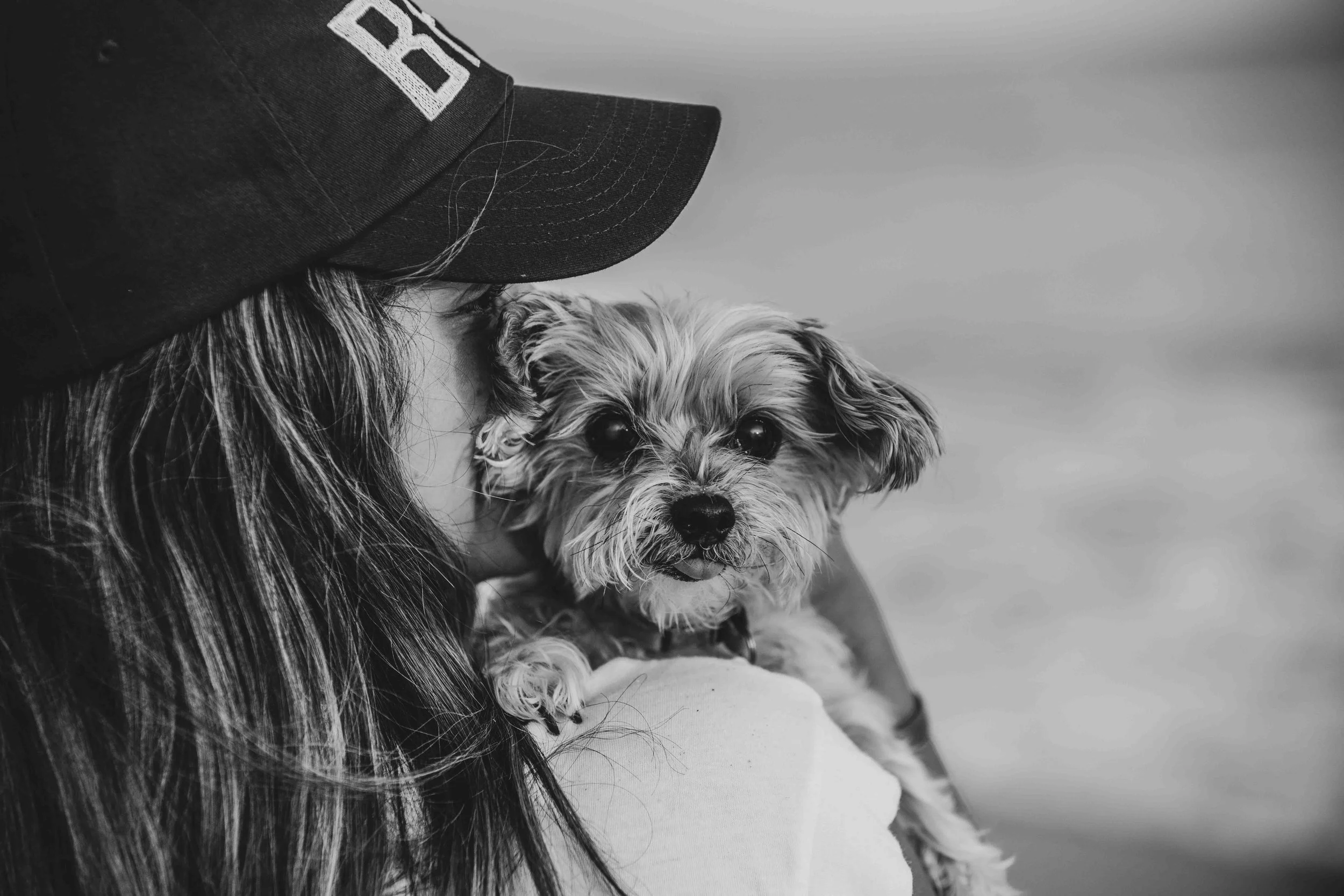 Person in a black cap cuddling a small shaggy dog in a black-and-white portrait