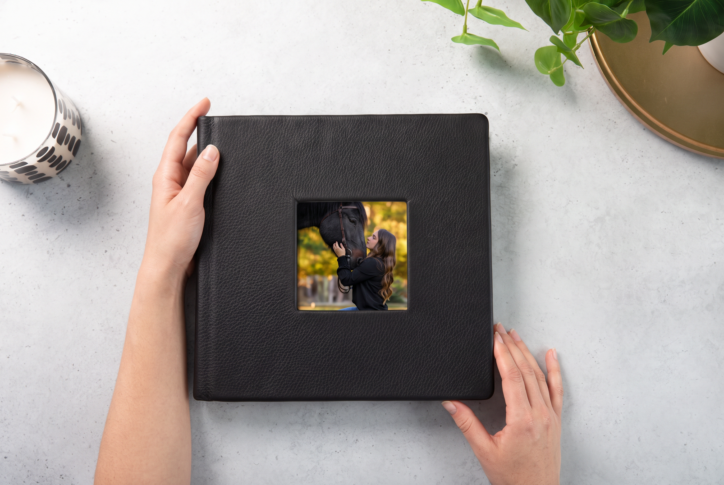 Hands holding a black leather photo album featuring a woman embracing a black horse