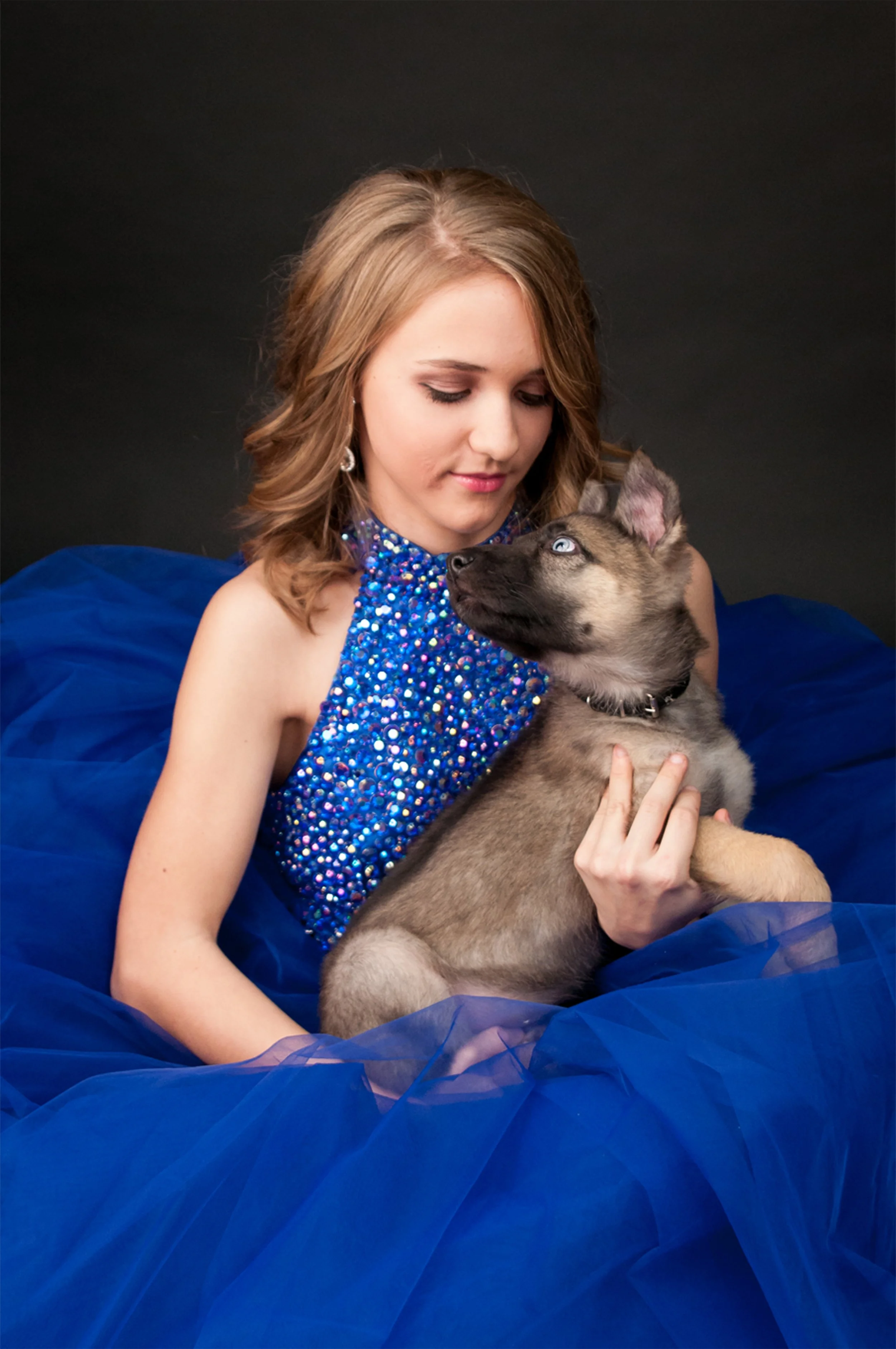 Woman in a blue sequined dress holding a small gray puppy against a black background