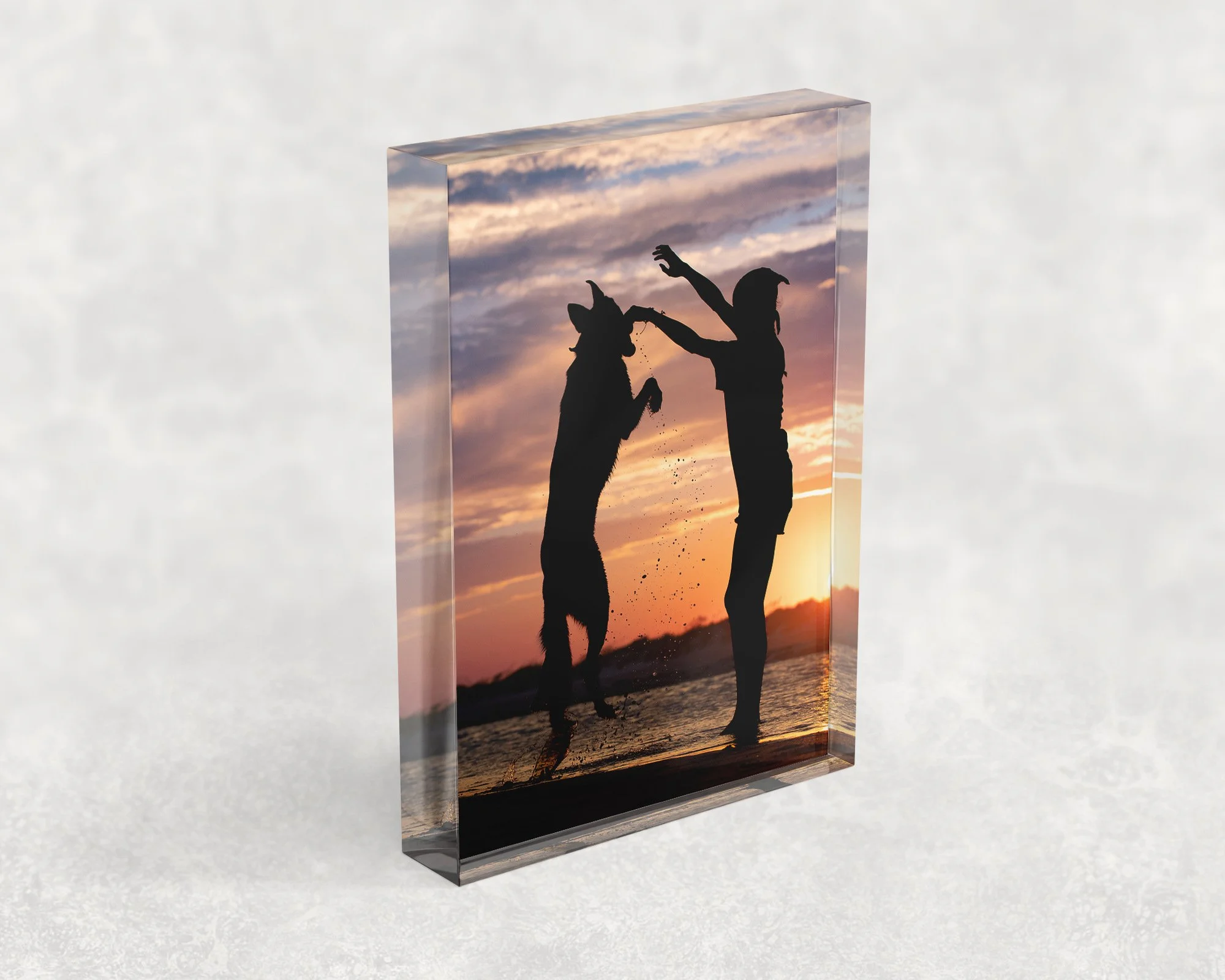 Freestanding acrylic photo block showing the silhouette of a dog jumping up to a woman at sunset on the water