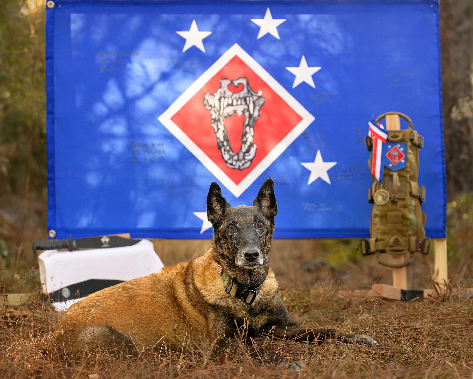 Cri lying in front of a flag signed by his fellow Marines, with his service vest, medal, and award knife beside him.