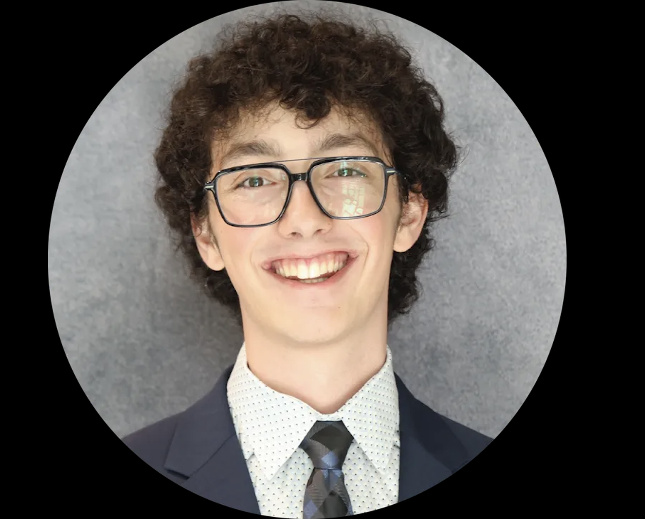 Smiling person with curly hair and glasses wearing a tuxedo, white dress shirt, and bow tie, with a gray background.