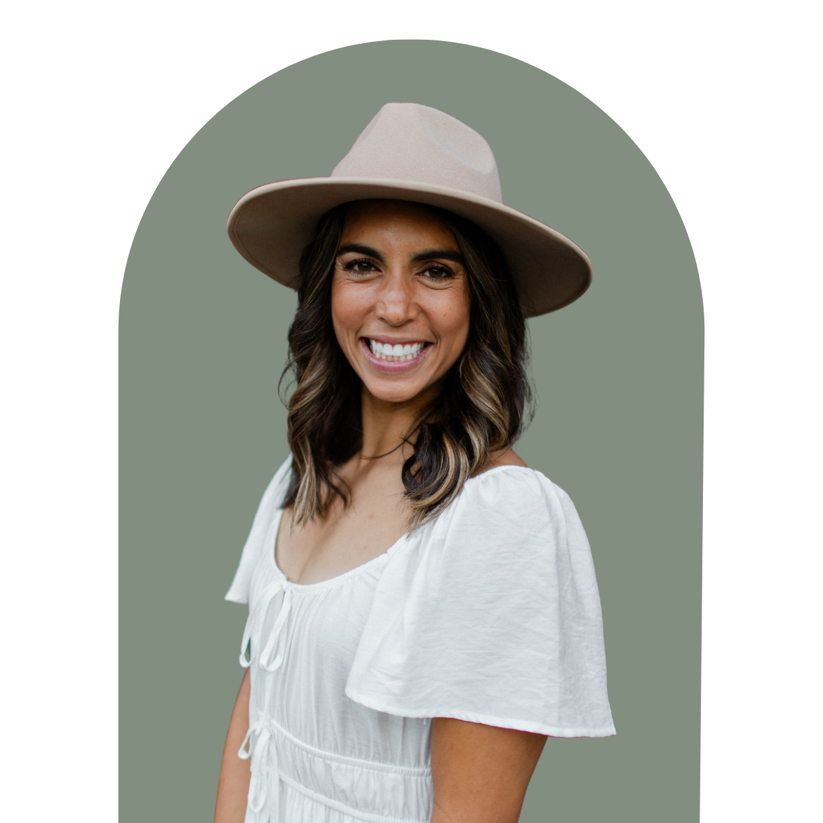 Smiling woman with wavy brown hair wearing a beige wide-brim hat and a white dress.