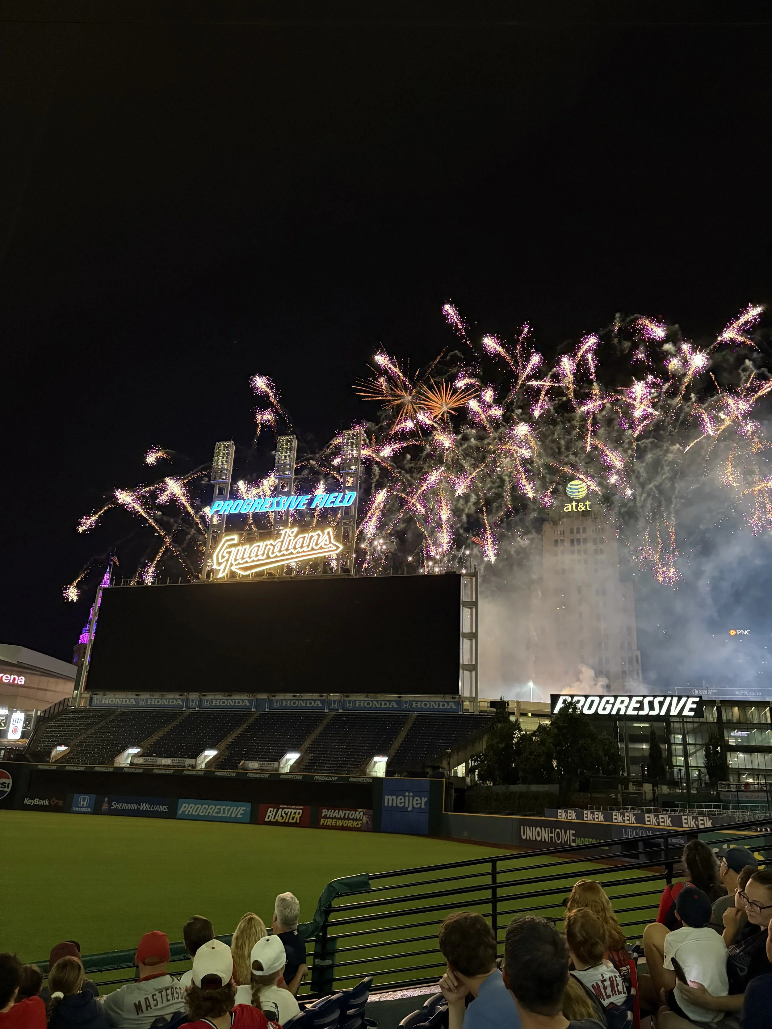 Fireworks exploding over a baseball stadium named Progressive Field, home of the Cleveland Guardians, with spectators watching from the stands.