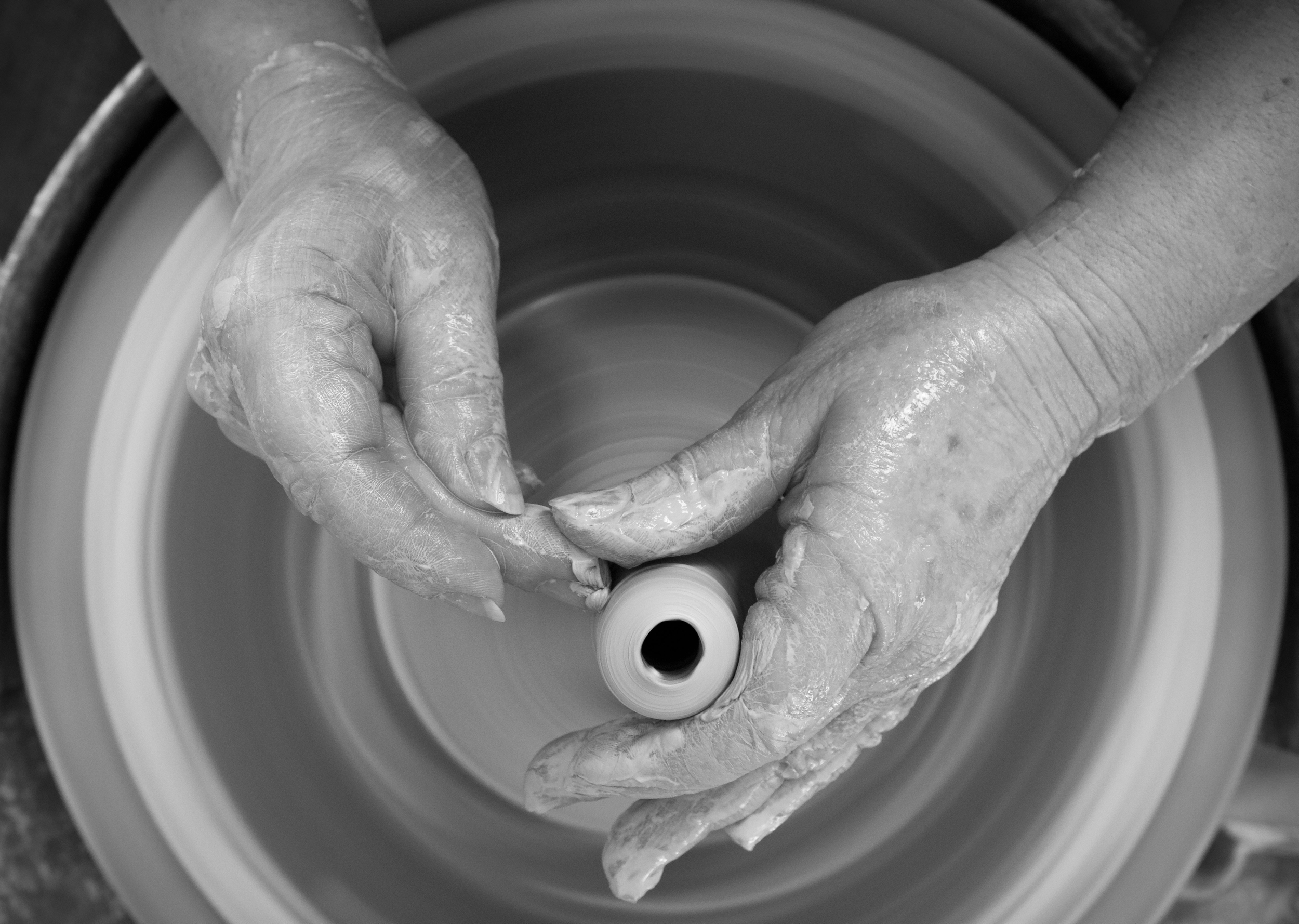 Close-up of a person's hands shaping a piece of pottery on a spinning pottery wheel.