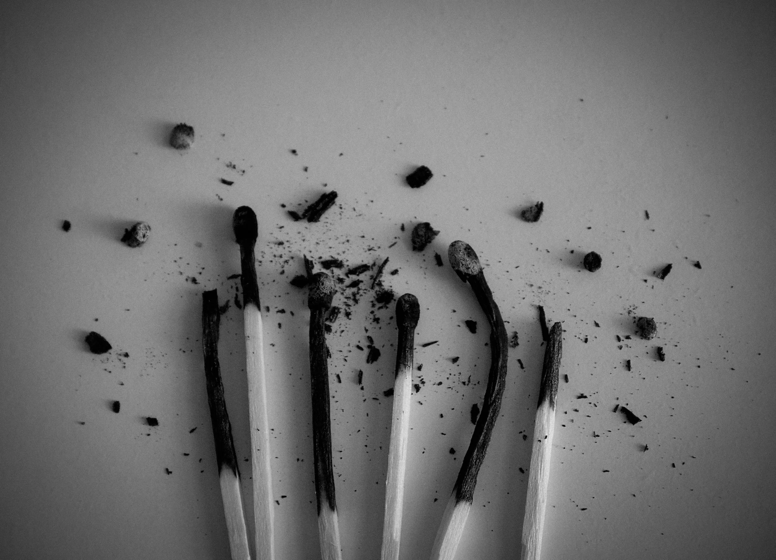 Blackened matchsticks with burnt tips and scattered black debris on a light background.