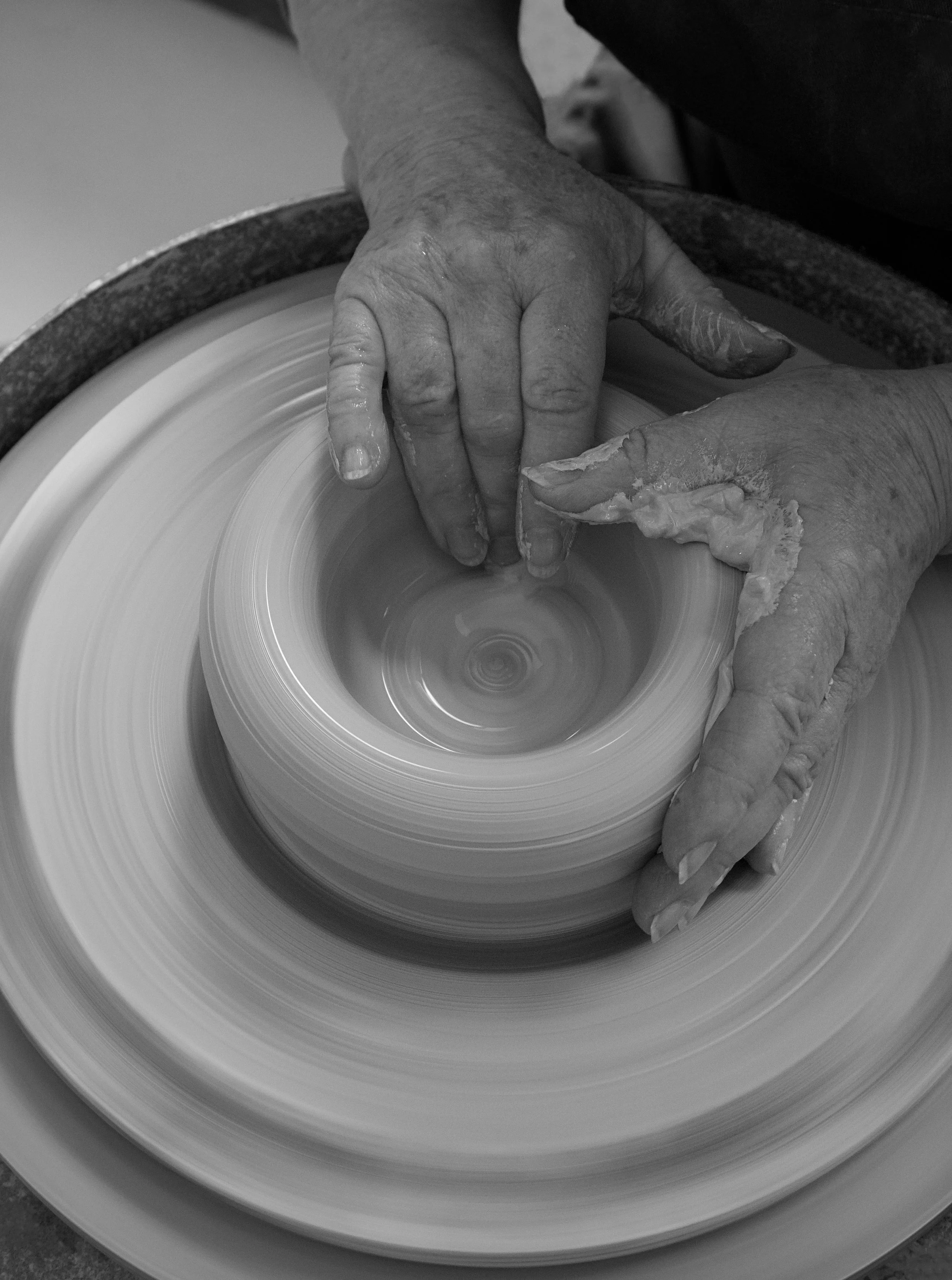 Hands shaping clay on a spinning pottery wheel.