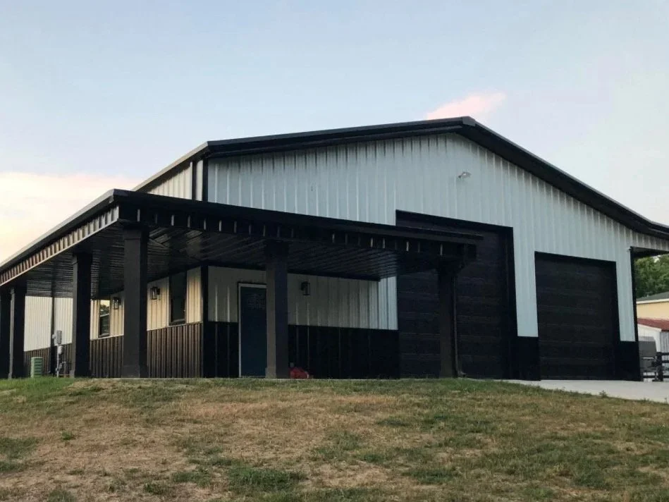 A large metal building with a black and white color scheme, a garage door, and a small porch with a roof supported by beams.