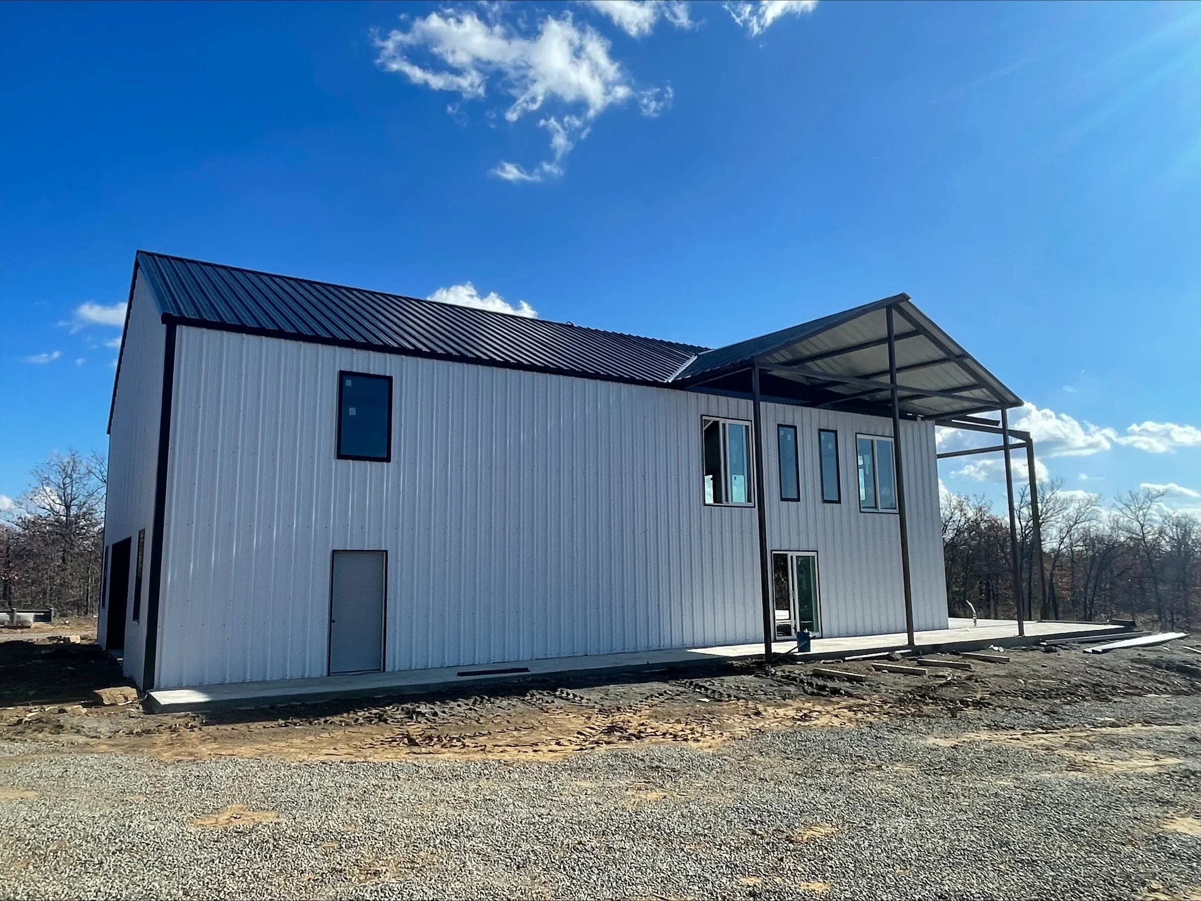 New building under construction with metal siding and a partly covered structure, set against a blue sky with clouds.