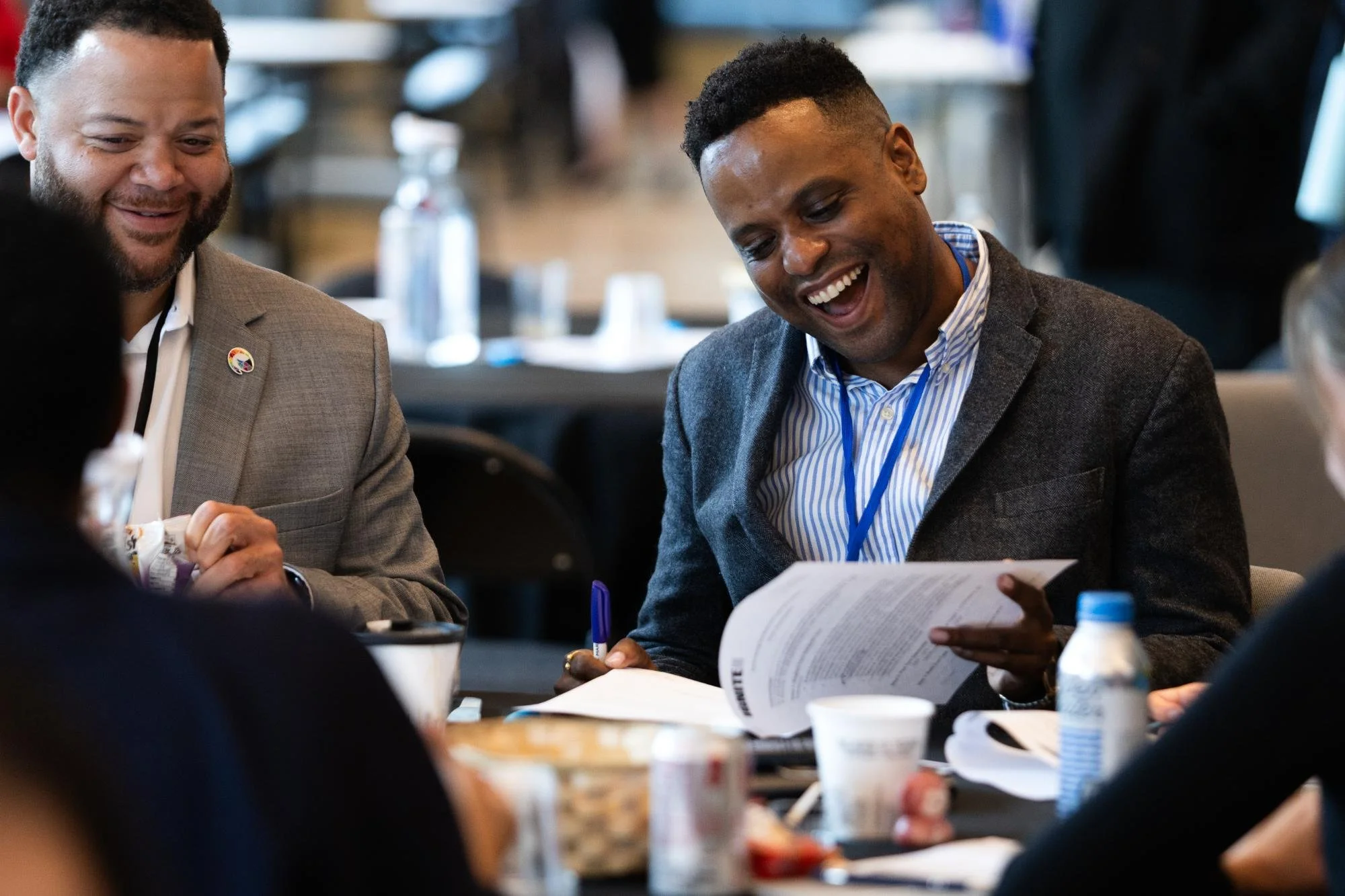 A Black man wearing a suit laughs while looking through a stack of papers