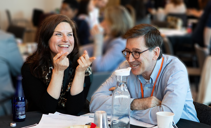 A woman and a man are smiling and engaging in conversation at a conference or meeting.