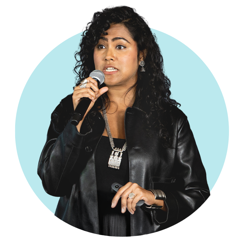 A brown-skinned woman with black curly hair speaks into a microphone