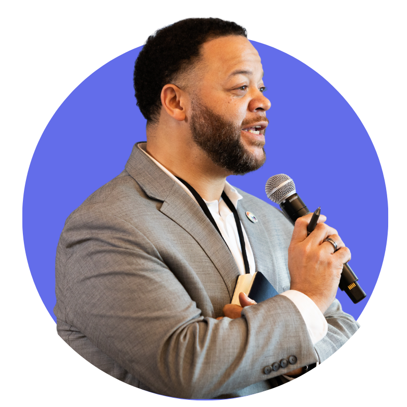 A Back man in a suit speaks into a microphone