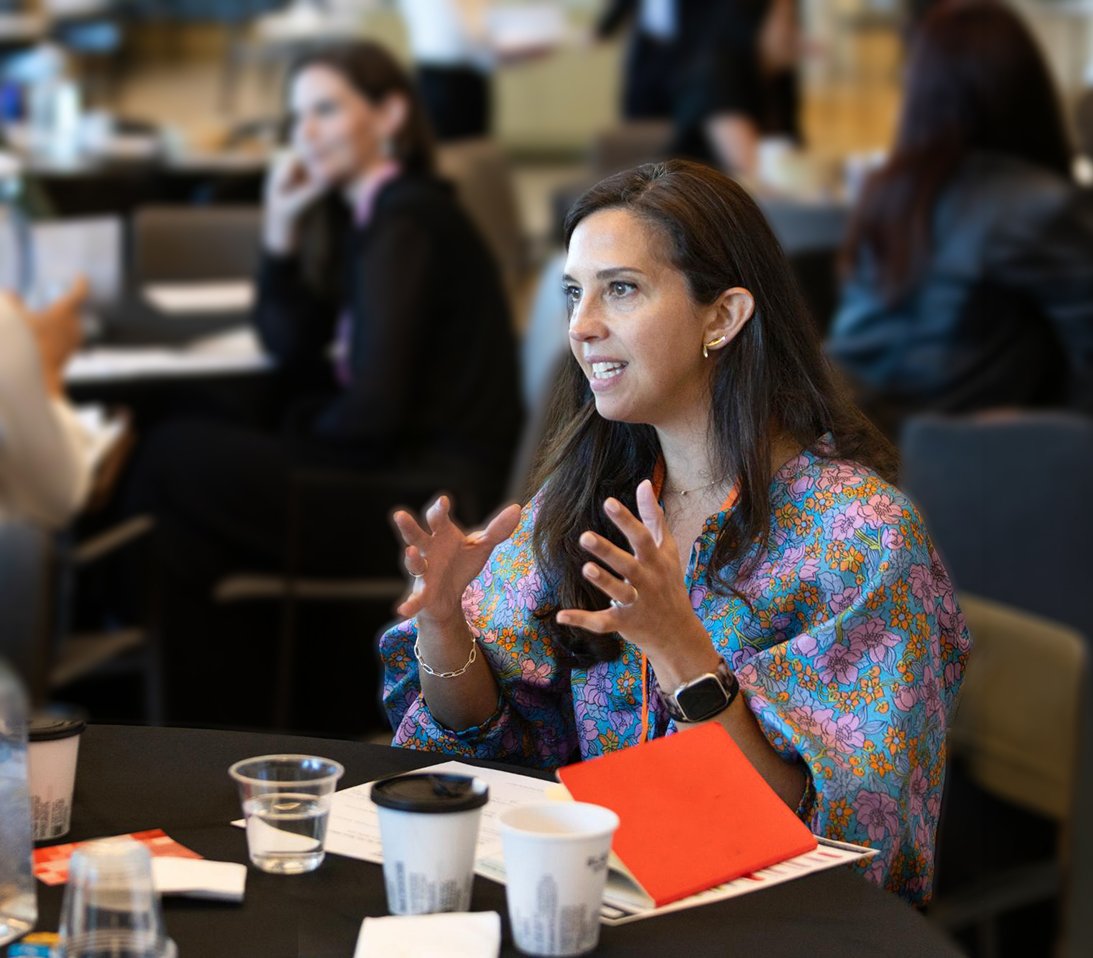 A brown-skinned woman with long dark hair gestures excitedly mid-speaking
