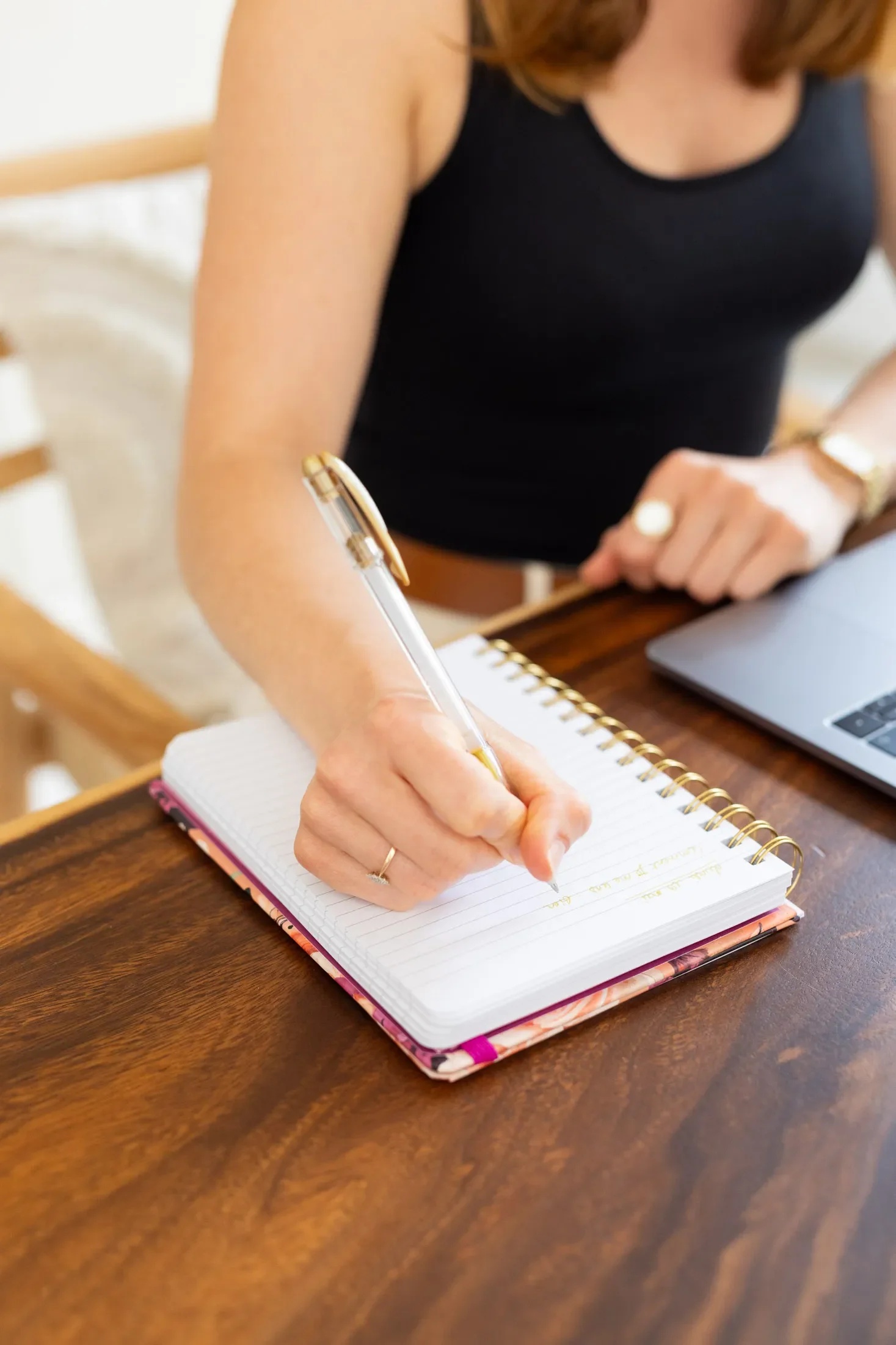 La fondatrice de Signature Stratégie qui écrit une plateforme de marque dans un carnet en posant sa main sur une table en bois, avec un ordinateur portable à côté.