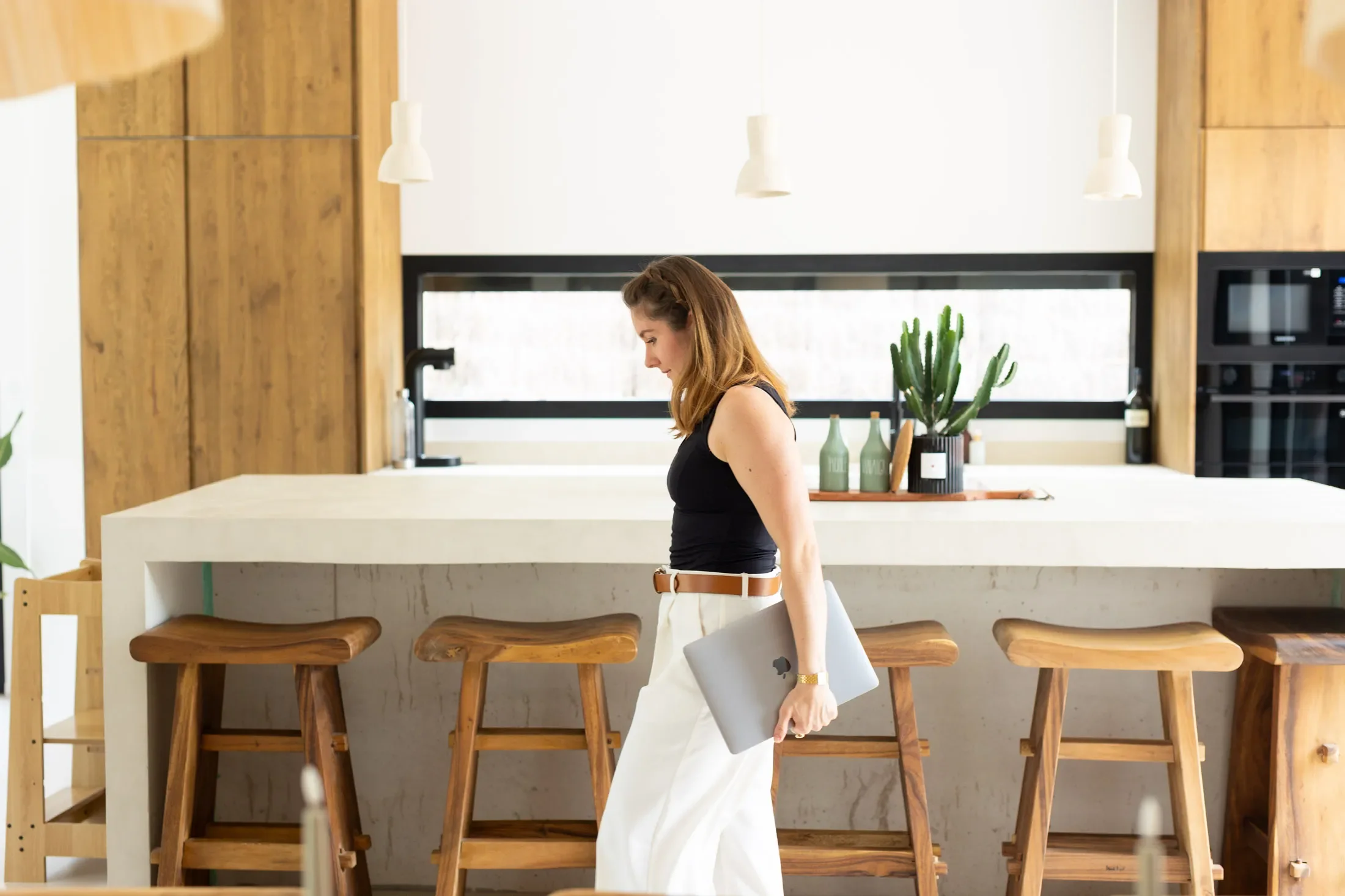 La créatrice de la méthode Image Rentable debout dans une cuisine moderne en bois, tenant un ordinateur portable qui part faire des photos chez un client.