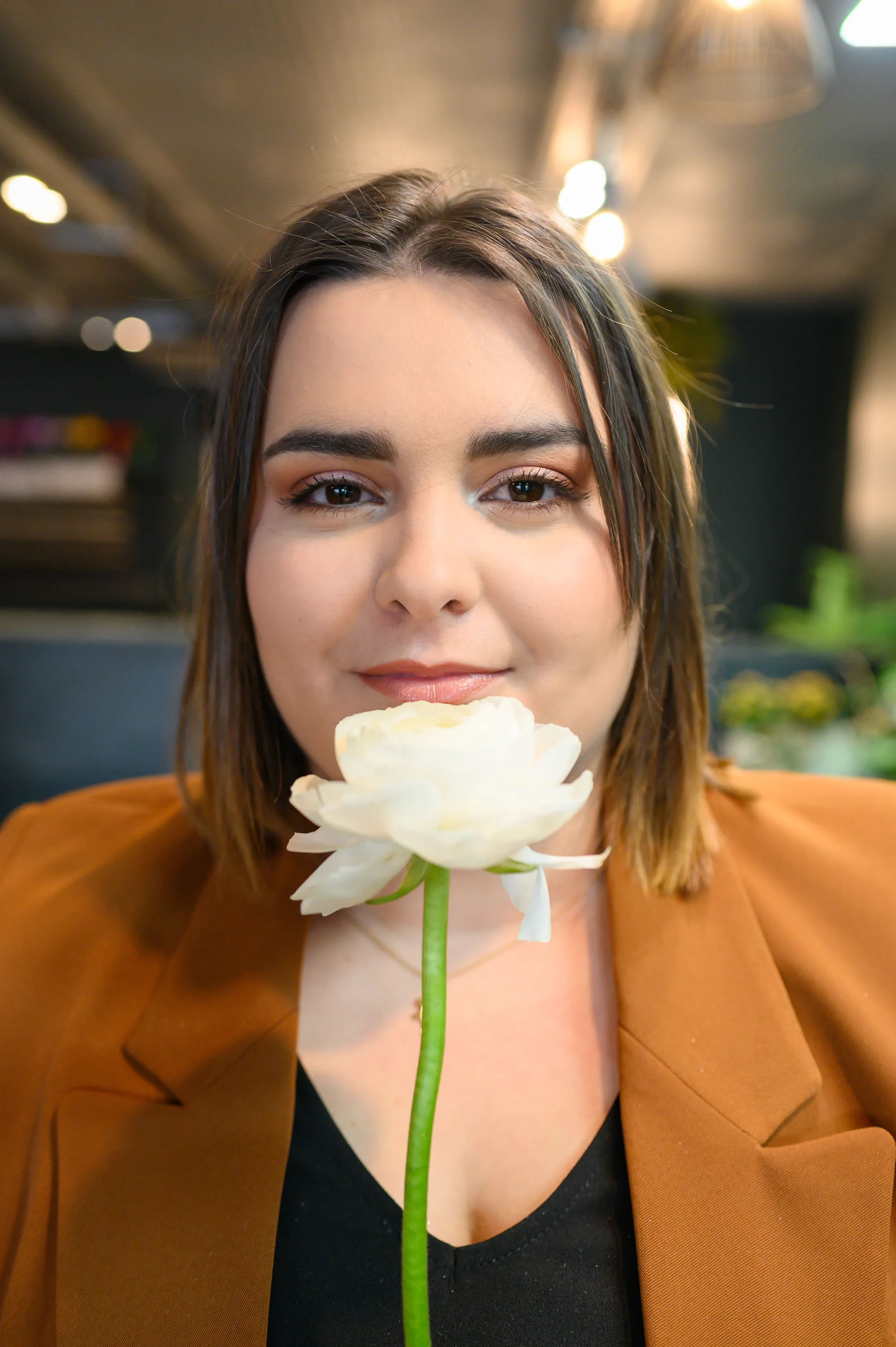 Portrait créatif d'une entrepreneure en veste terracotta tenant une rose blanche, photographie professionnelle affirmant son identité visuelle.