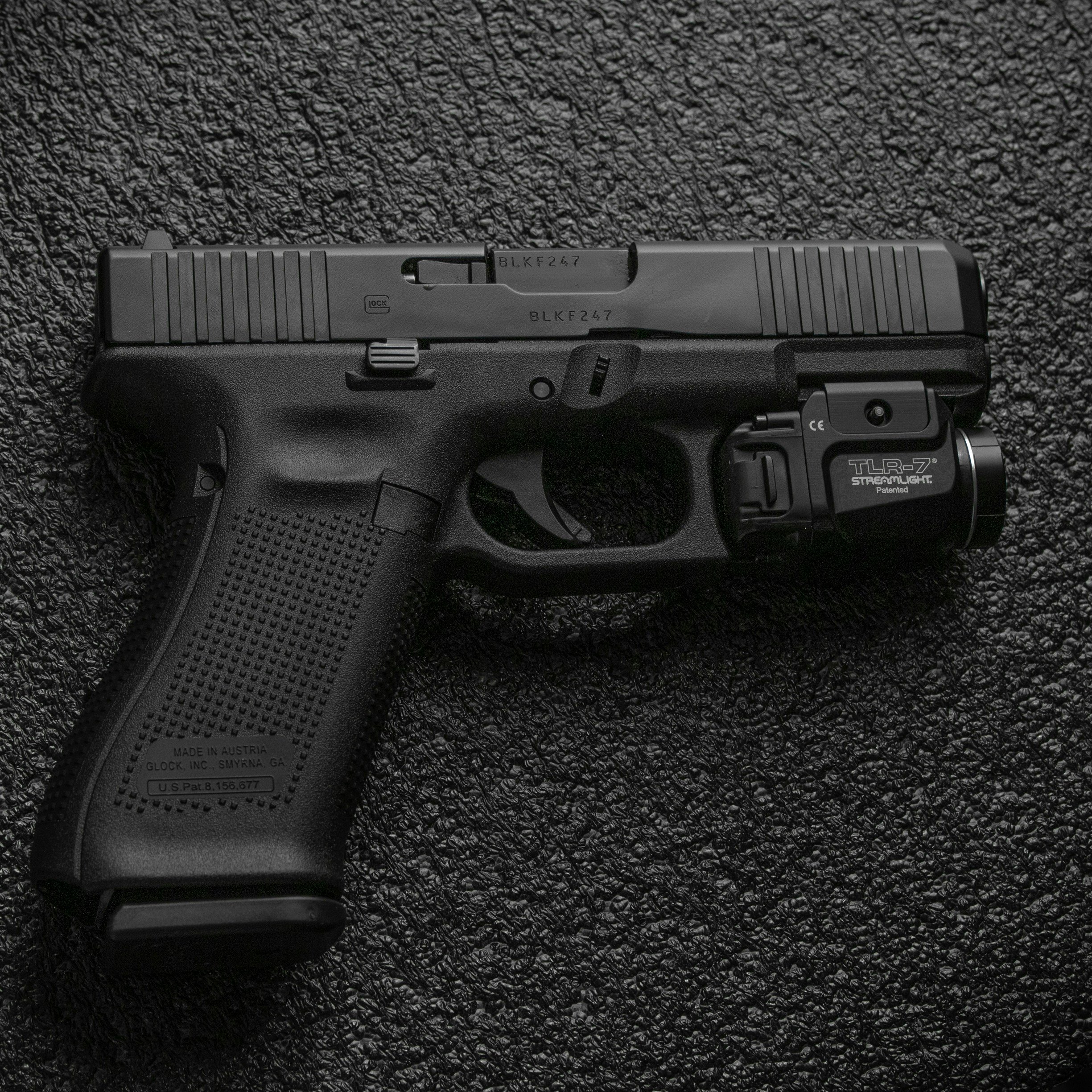 Close-up of a black Glock handgun placed on a textured black surface, showing the slide with serial number and other markings. - AA Wholesale | Amory | MS | Wholesale | Deals | Amory Auction
