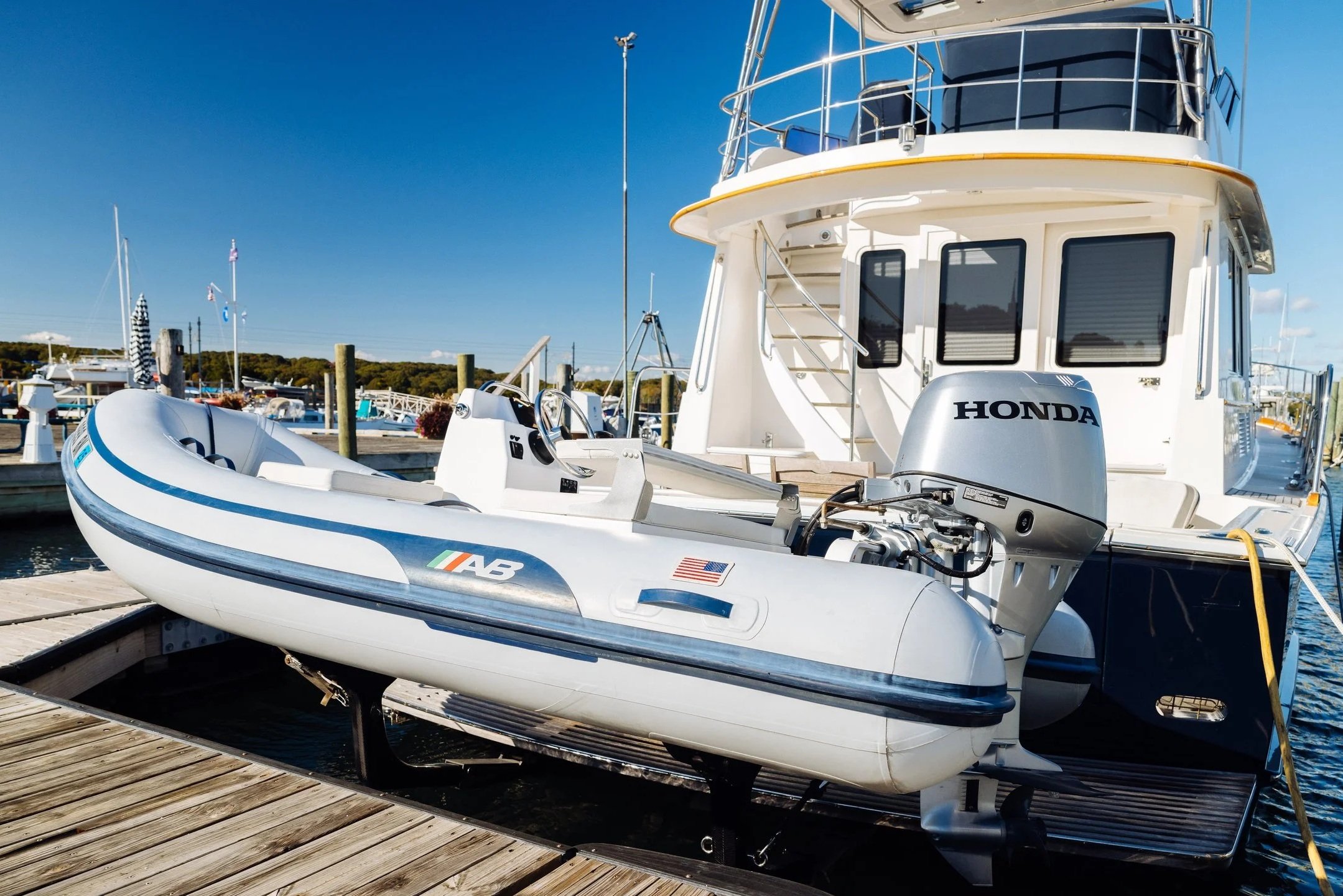 A white motorboat with a Honda outboard engine docked at a marina, with other boats and a clear blue sky in the background.
