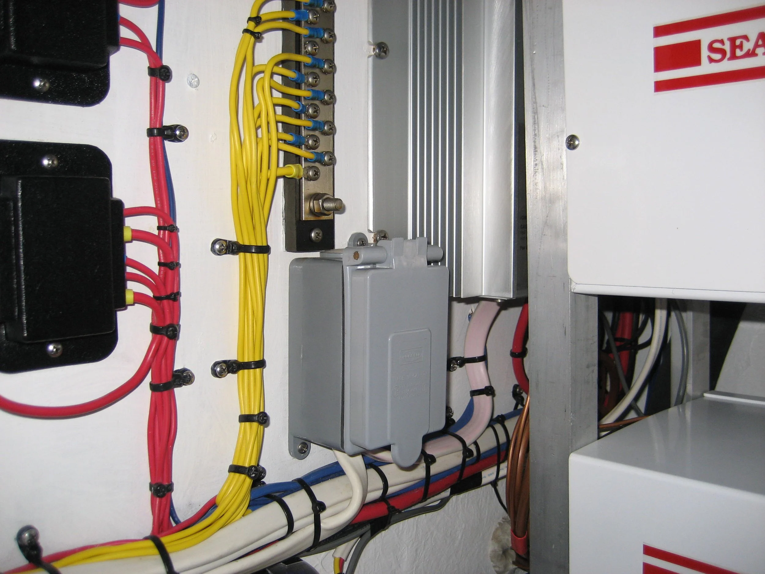 Electrical wiring inside an electrical panel or control box, with multiple colored wires, terminal screws, and a metal mounting plate.