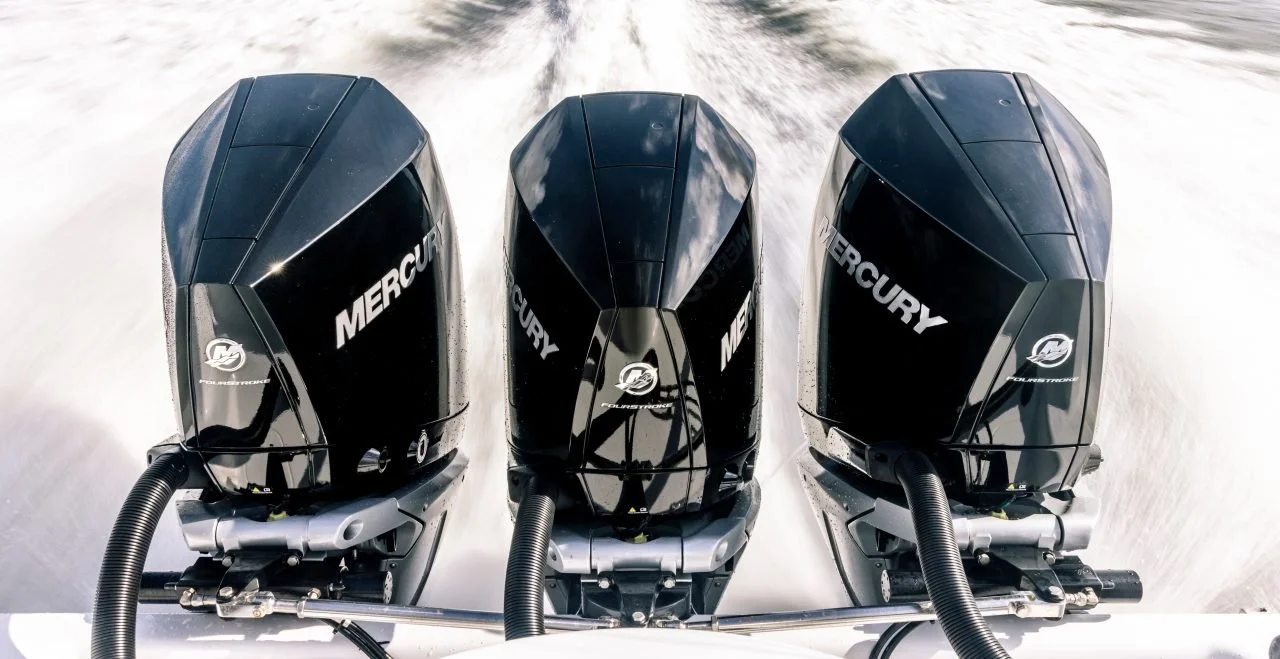 Three Mercury outboard motors mounted on a boat propelling through water.