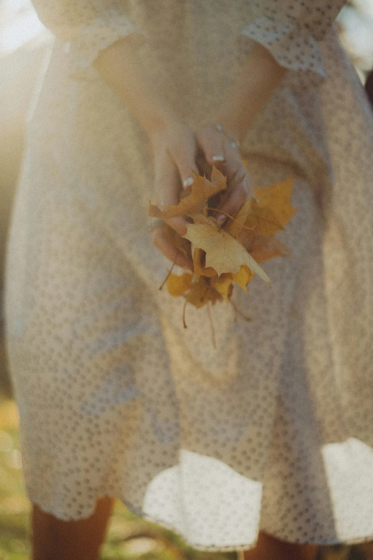 A person holding a handful of fallen autumn leaves while wearing a polka-dot dress.